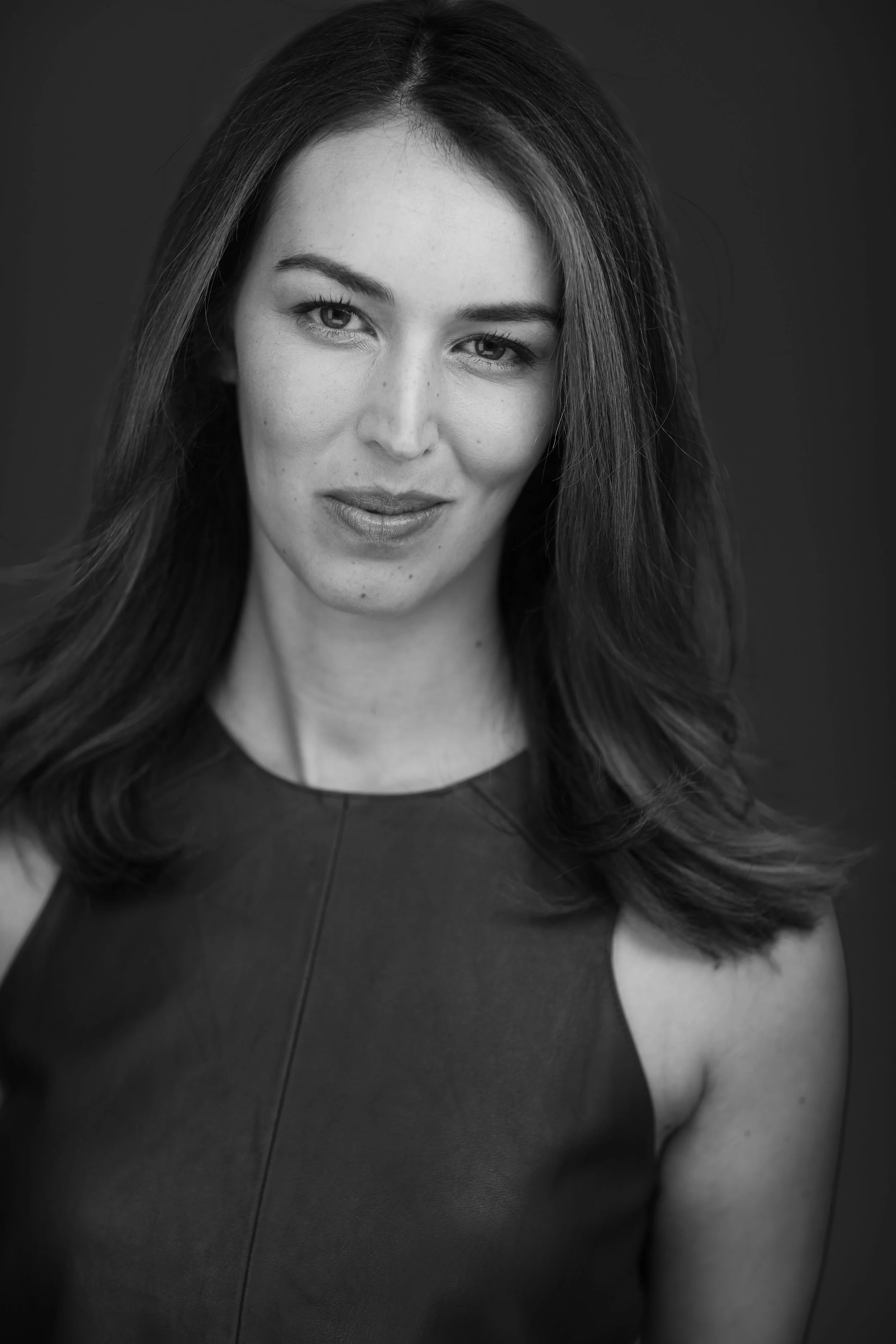 Black and white portrait of a woman with long hair, wearing a sleeveless top, smiling slightly and looking at the camera.