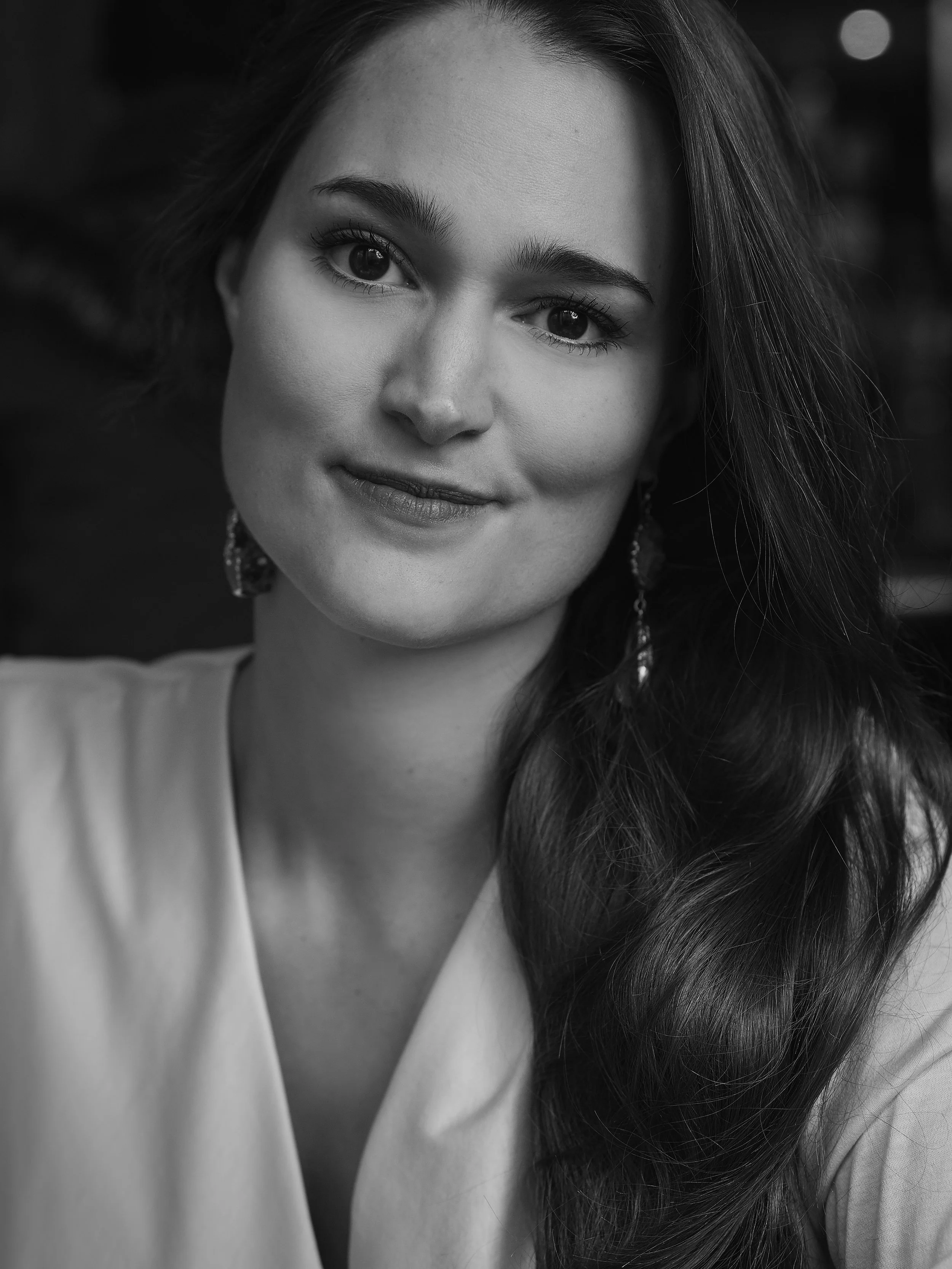 Black and white close-up portrait of a smiling young woman with long hair, wearing earrings and a light-colored top.