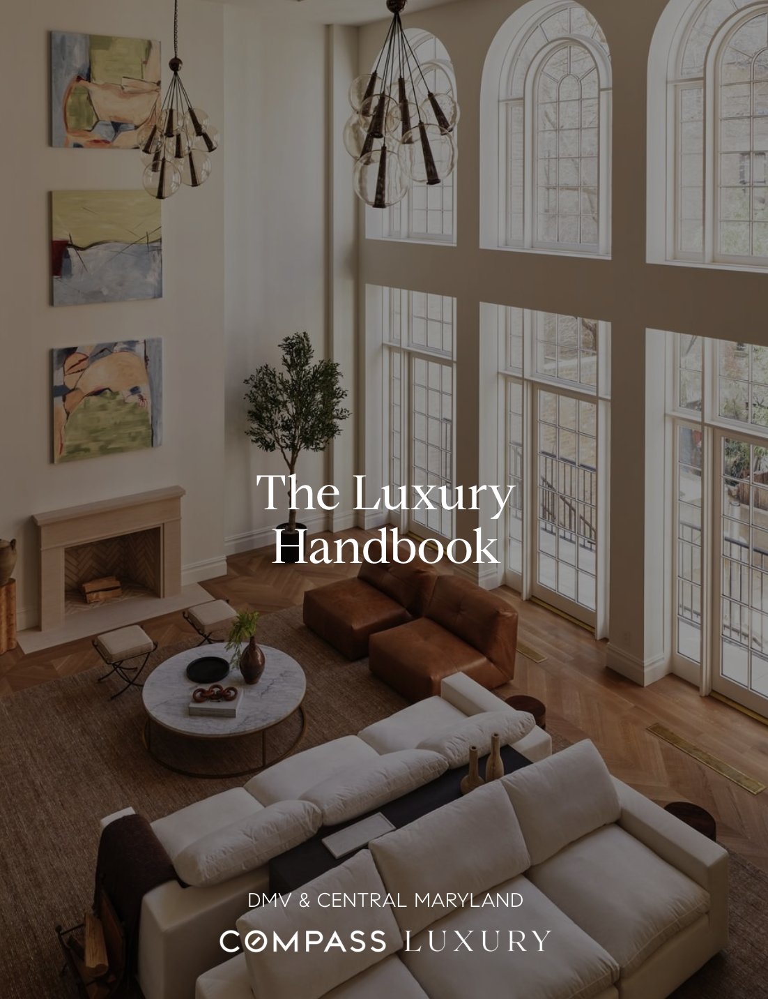 Elegant living room with high vaulted ceilings, large arched windows, modern chandelier, abstract paintings on the wall, tall potted plant, brown leather sofa, white sectional sofa, round marble coffee table with decorative items, and wooden flooring.