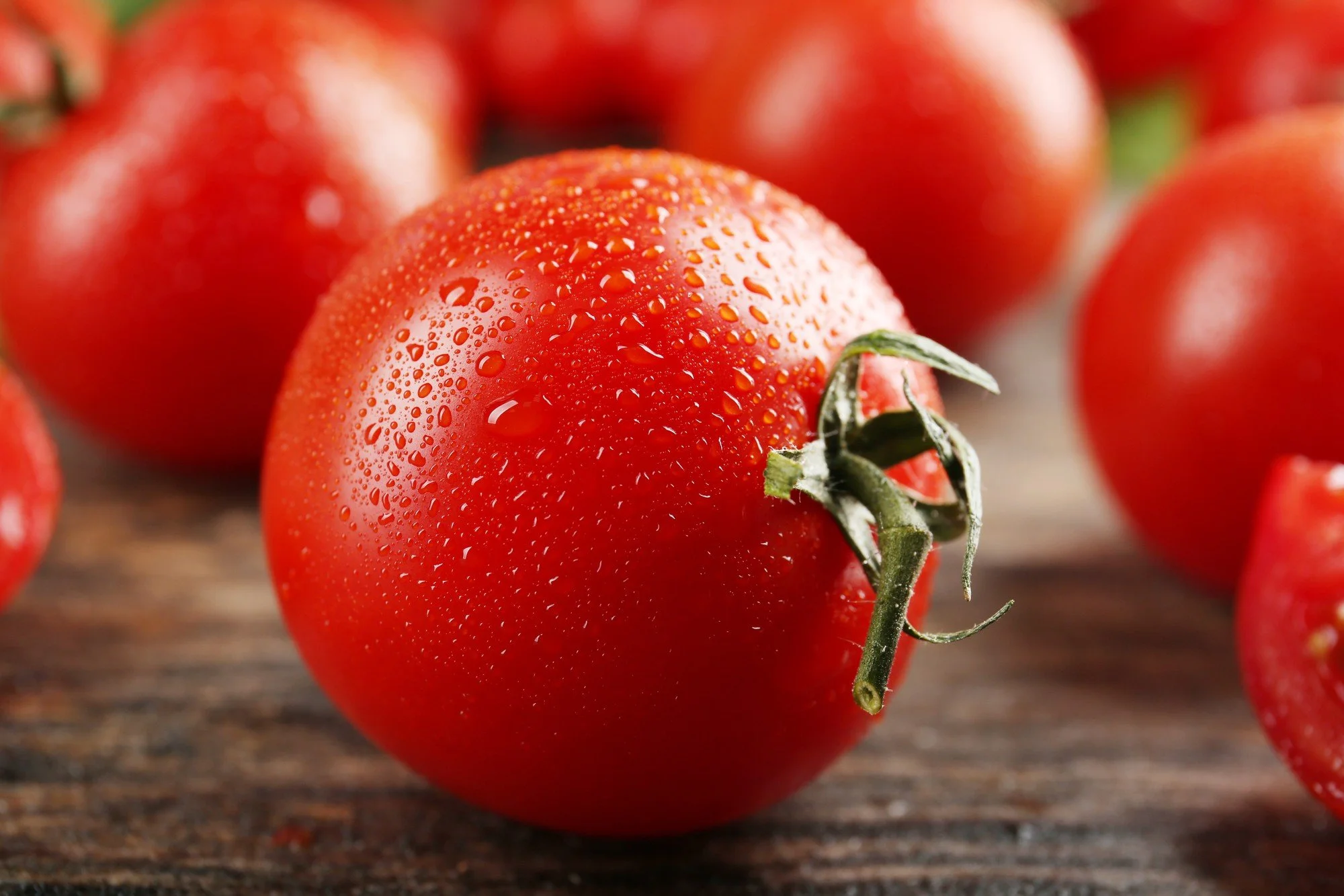 Tomates frescos con gotas de agua sobre una superficie de madera.