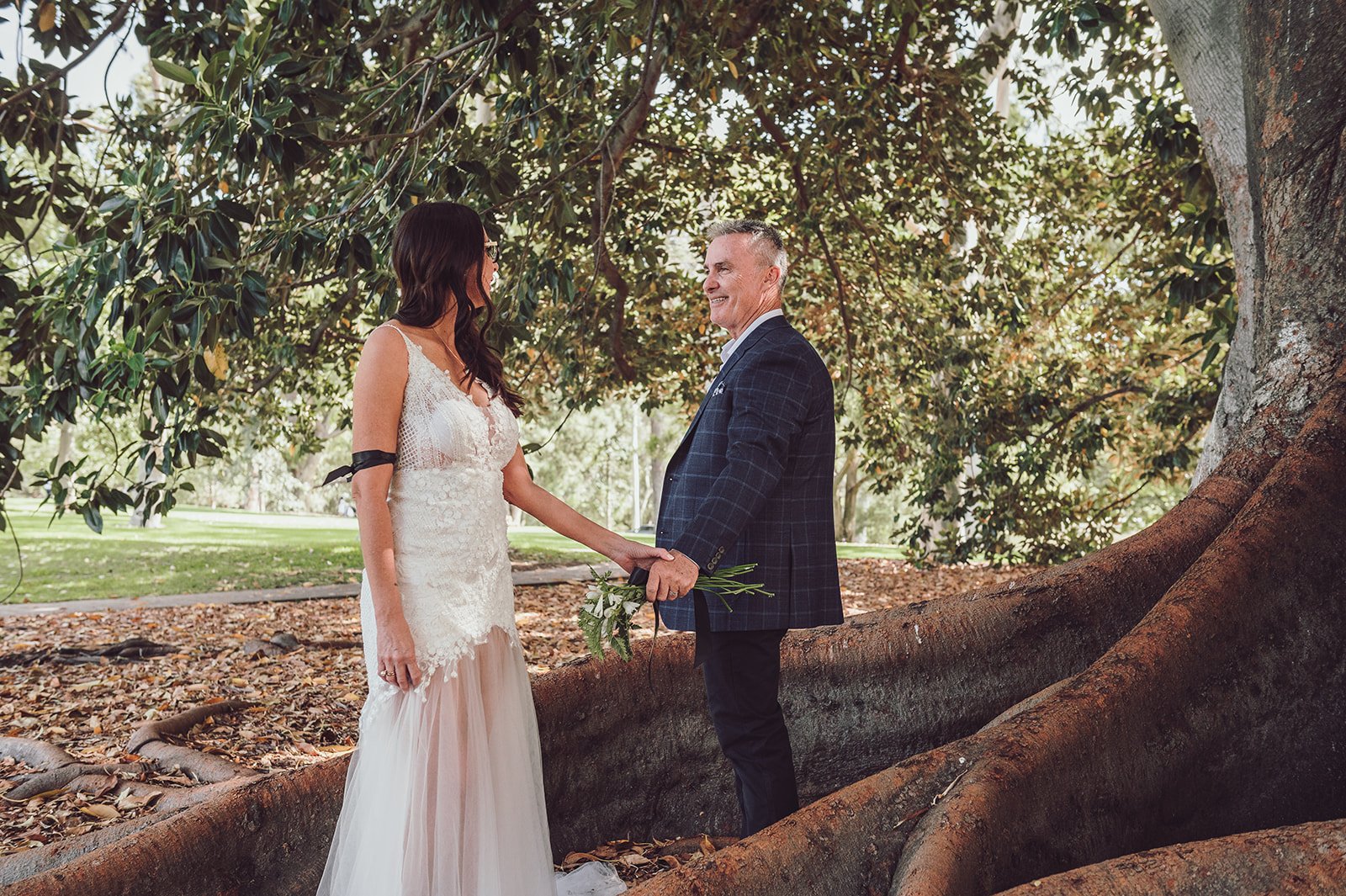 A bride and groom holding hands under a large tree during their wedding ceremony outdoors.