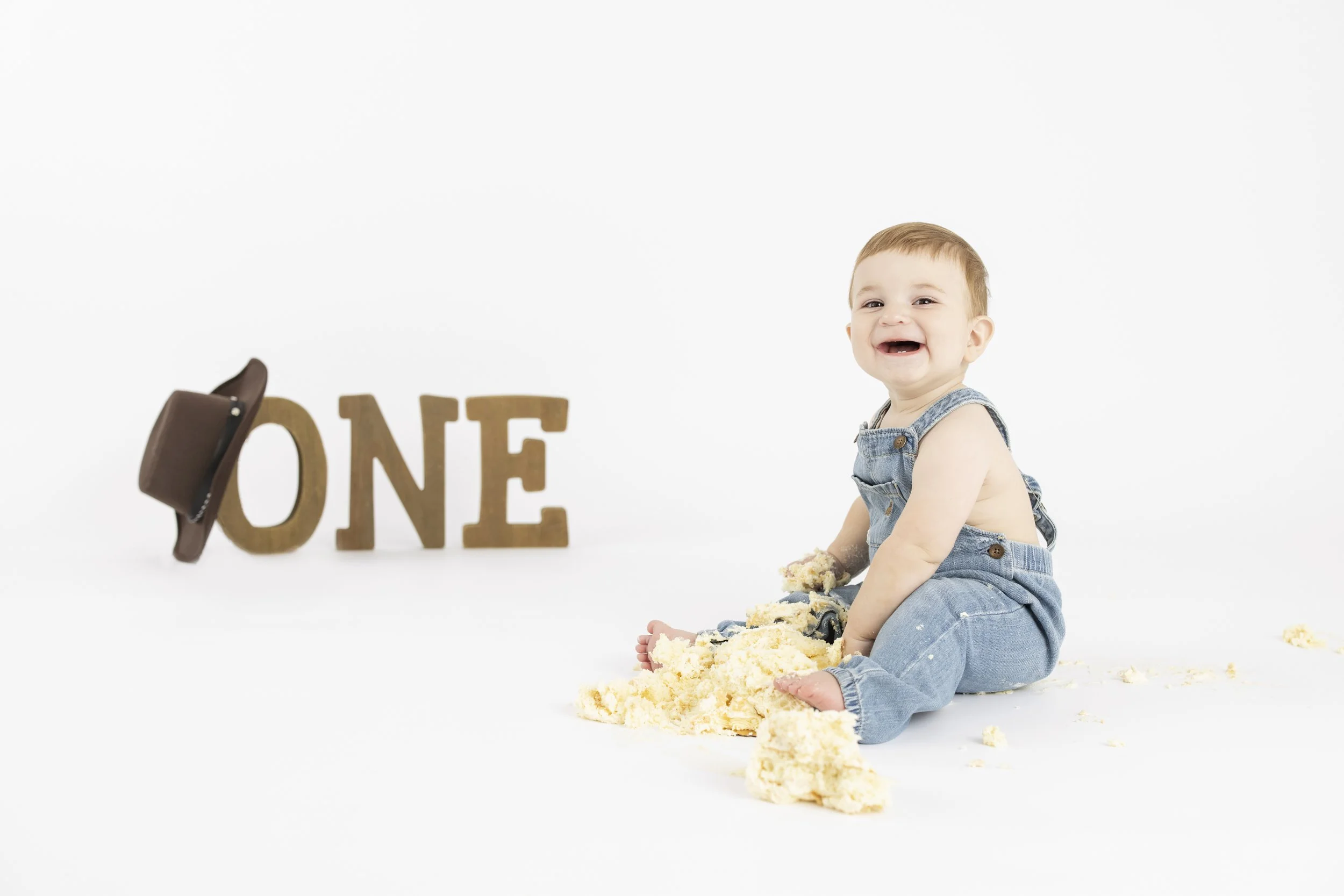 A one year old celebrates his first birthday with a cake smash on a white background