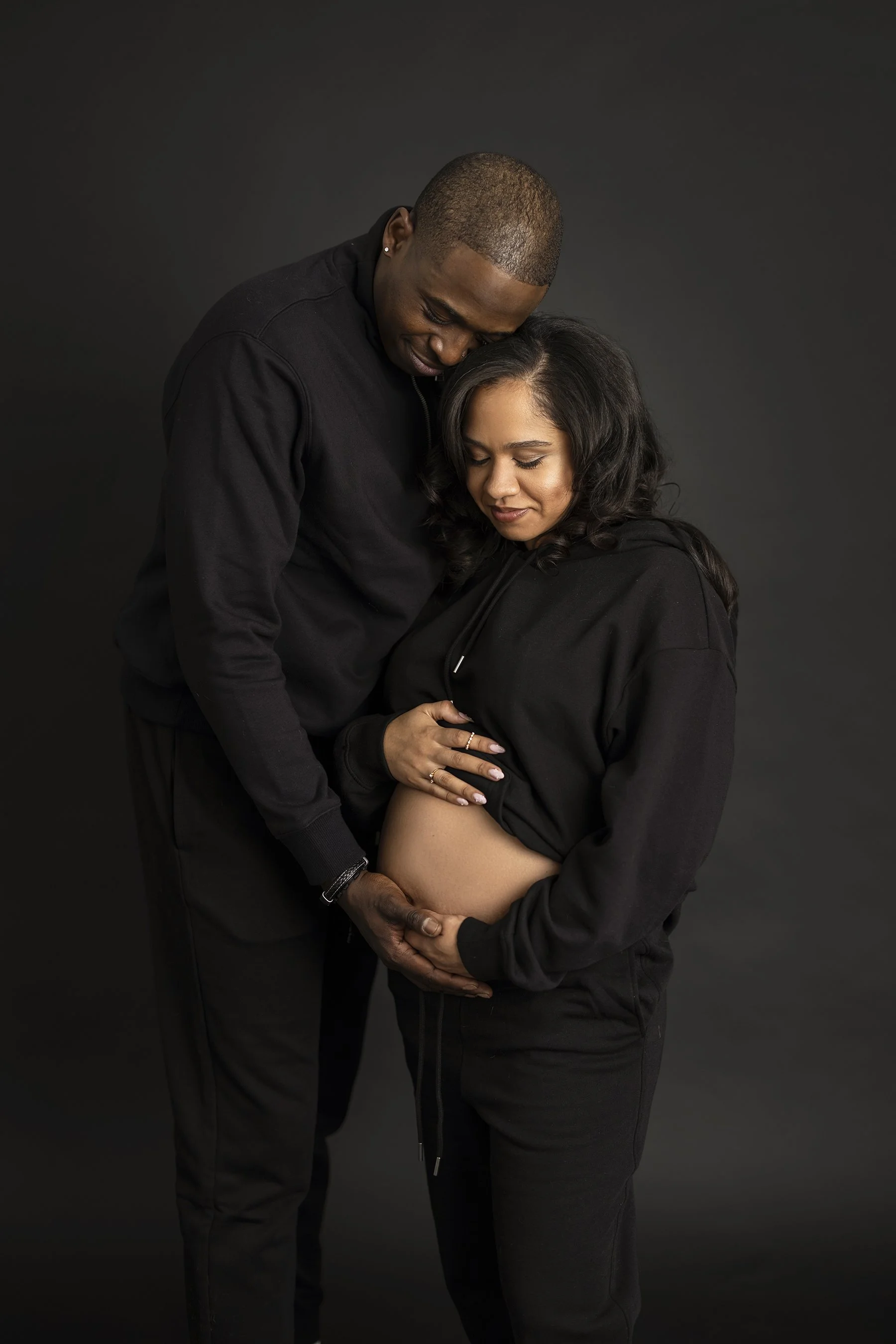 A couple has maternity photos taken on a black background