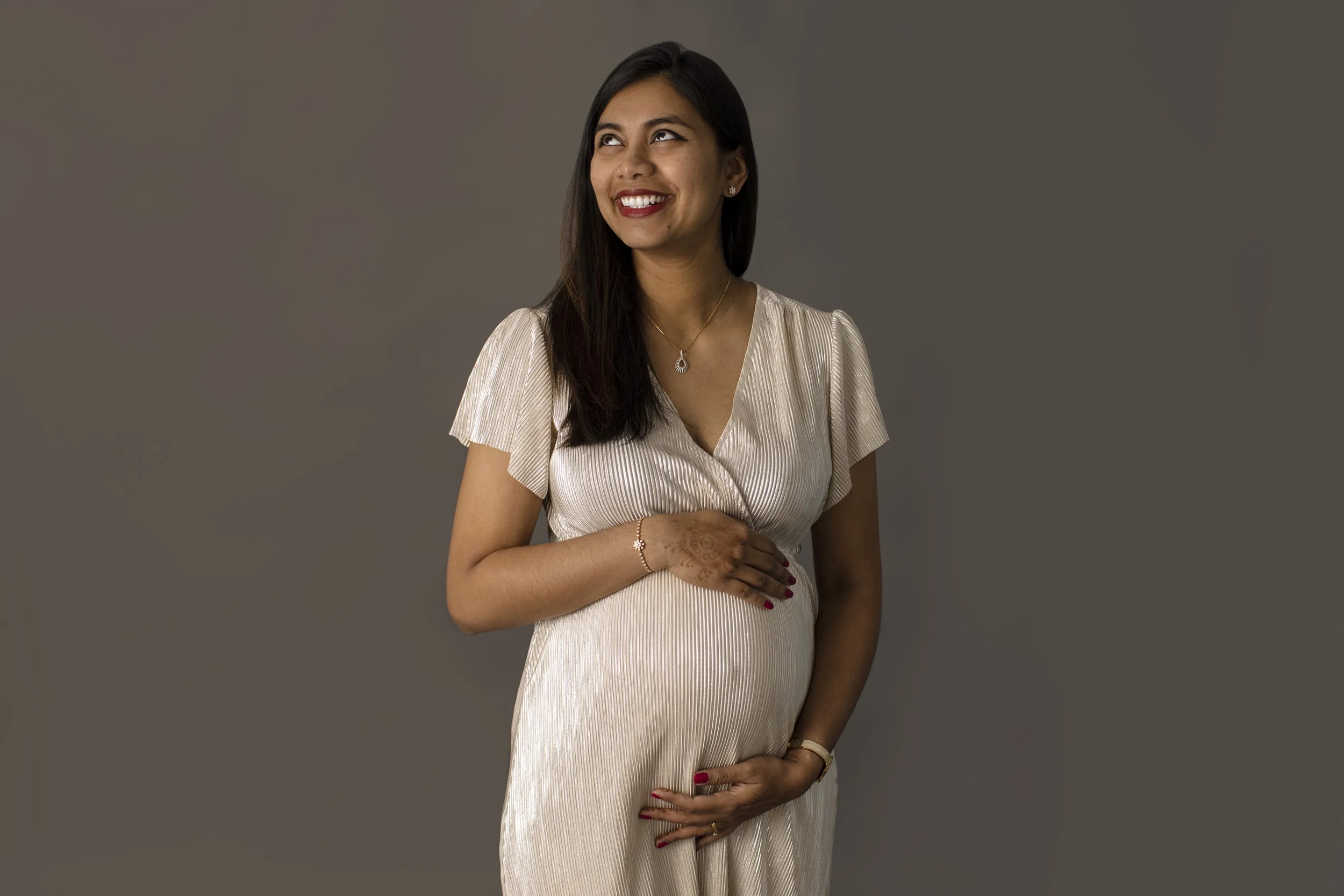 An expecting mother poses for maternity photos in front of a grey background