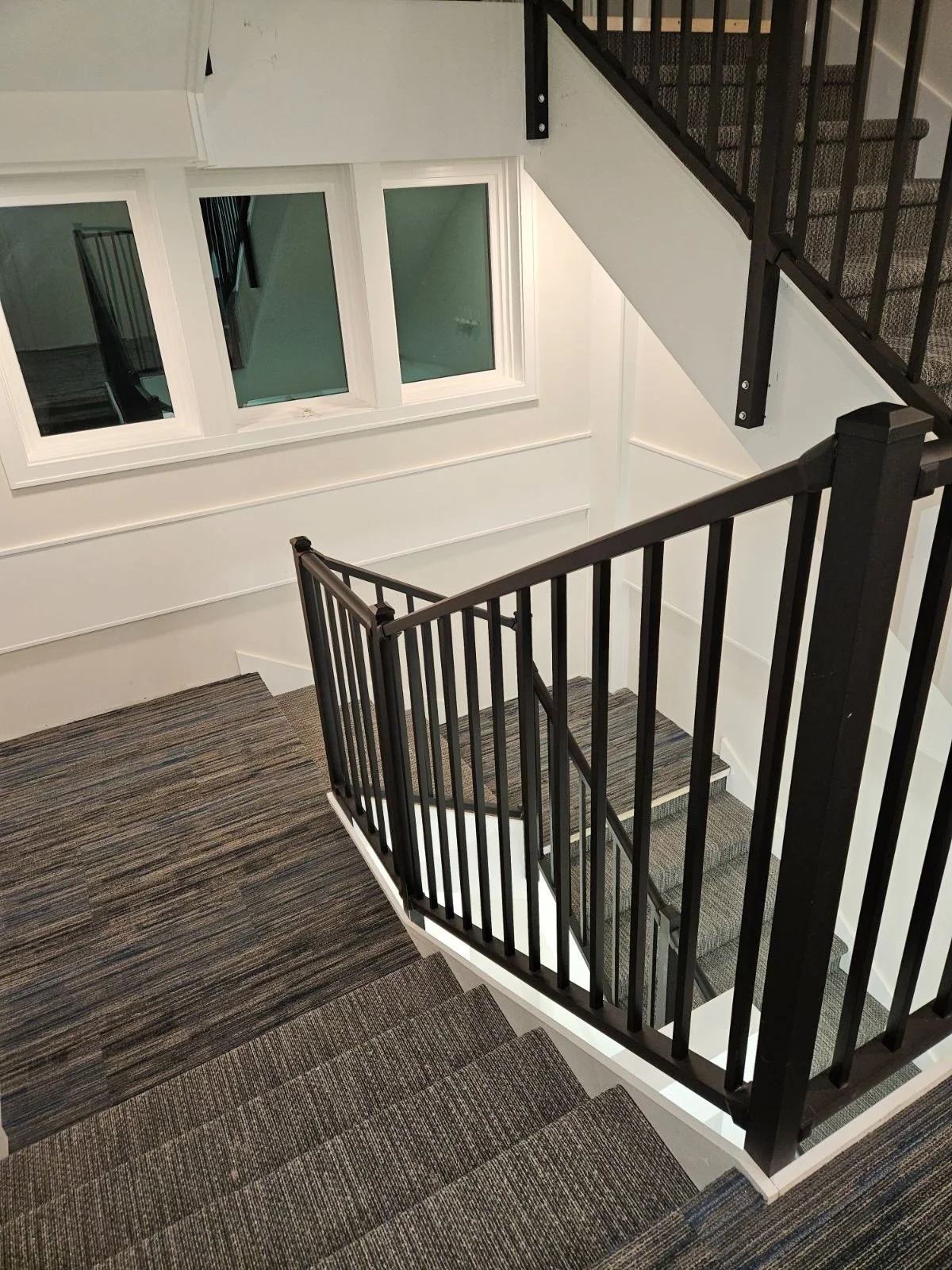 View of a staircase with black railing, wood and carpeted steps, and white walls and window frames.