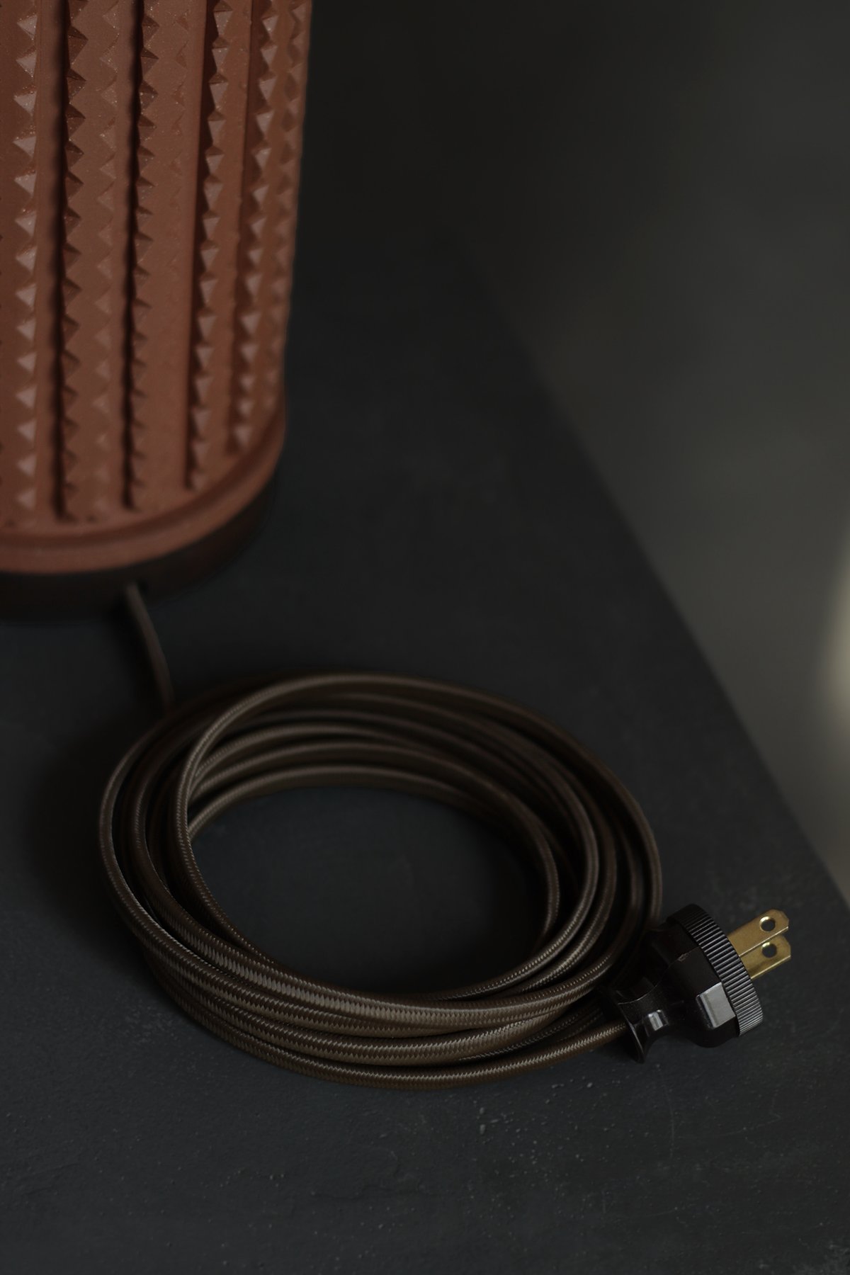 Close up detail of brown fabric lamp cord and terracotta ceramic base sitting on a table.