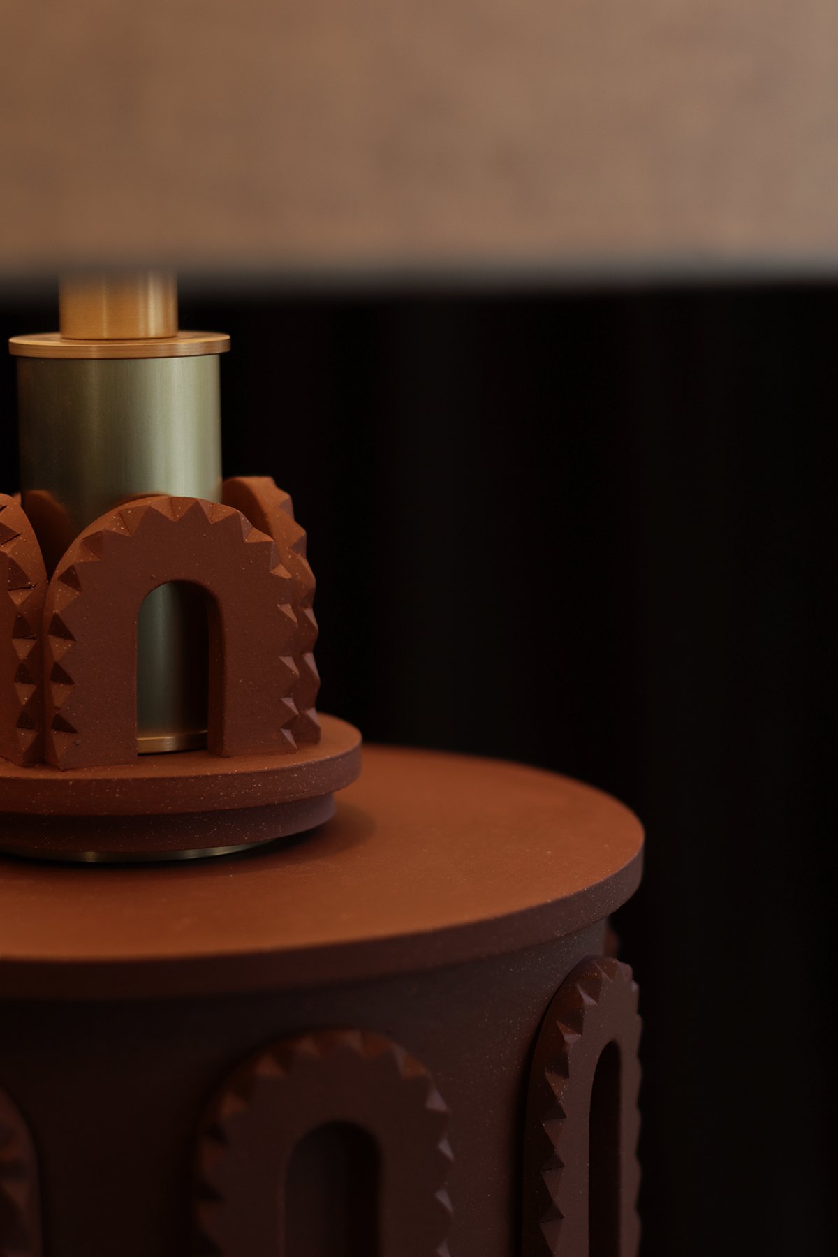 Close-up of a lamp base featuring hand carved clay with concentric triangular patterns and brass neck.