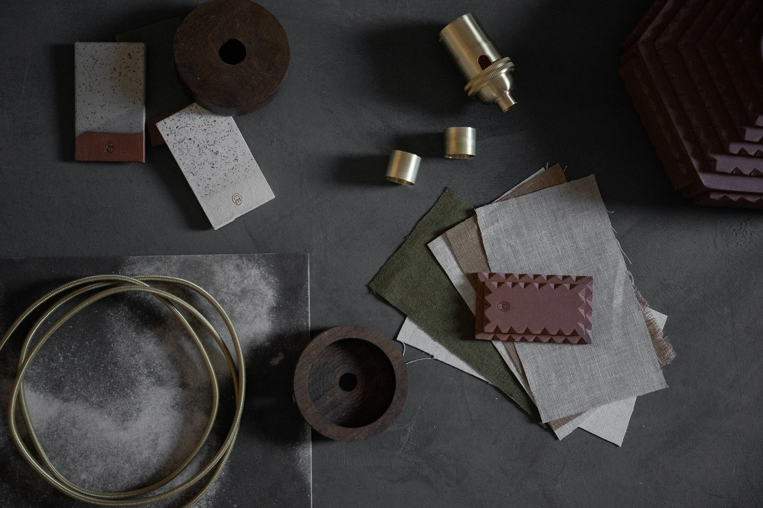 Design and interior decor materials including swatches of fabric, metal, and paper, along with metallic rings and decorative objects on a dark surface.