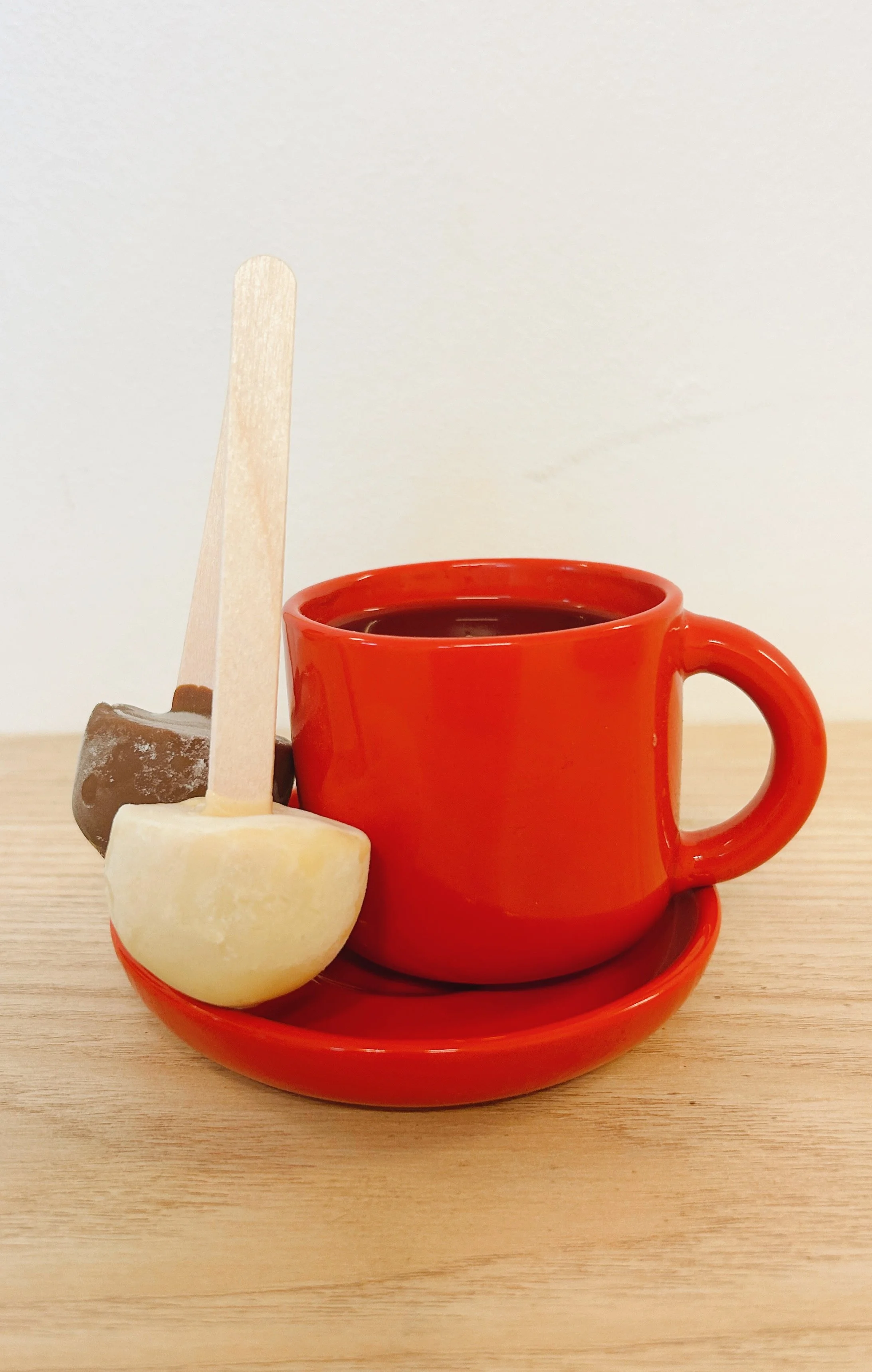 En röd kopp med kaffe på ett fat och tre julgodisar stående intill koppen.