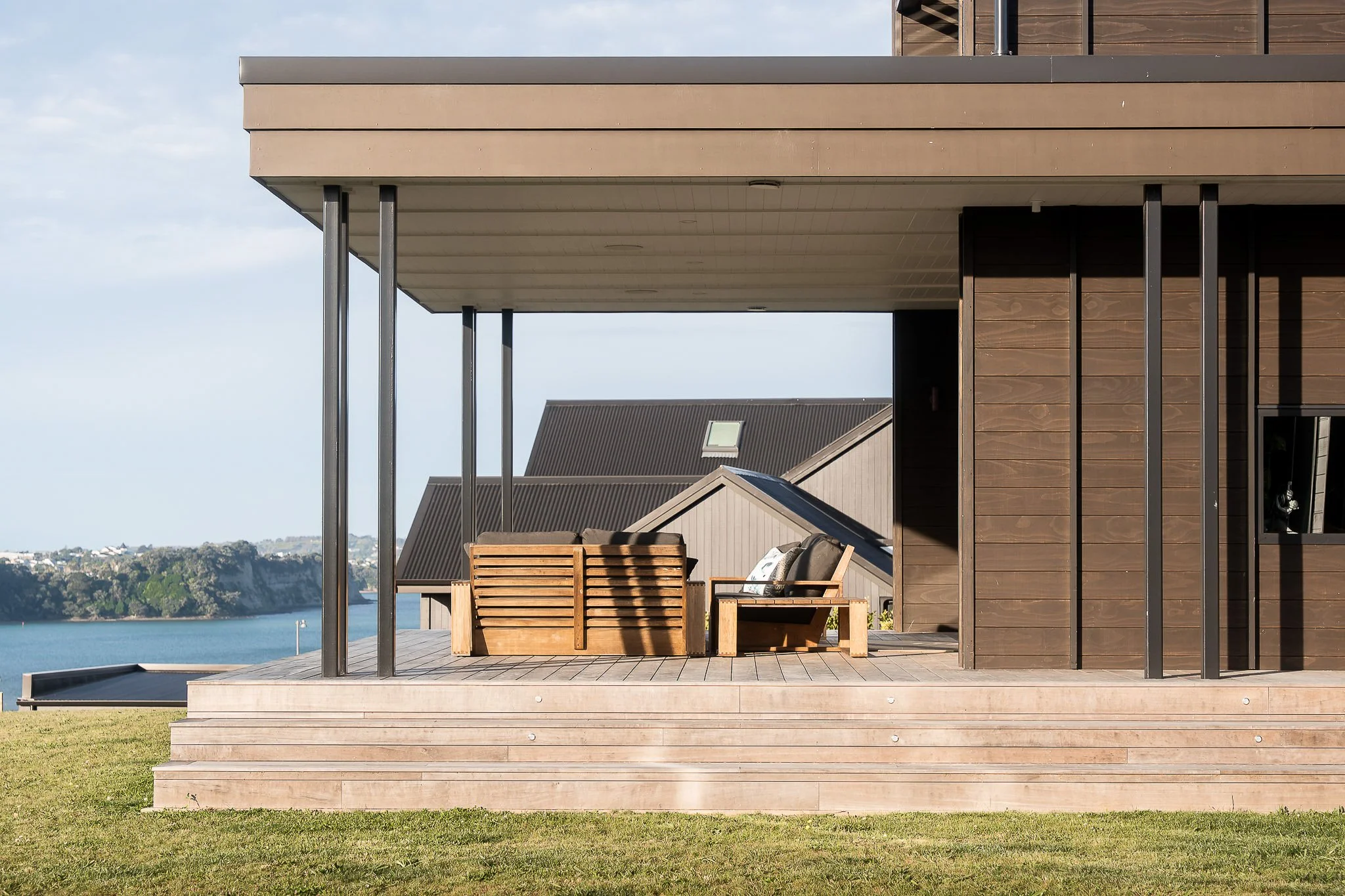 Architectural new build in Weiti Bay featuring a covered timber deck with outdoor seating and coastal views