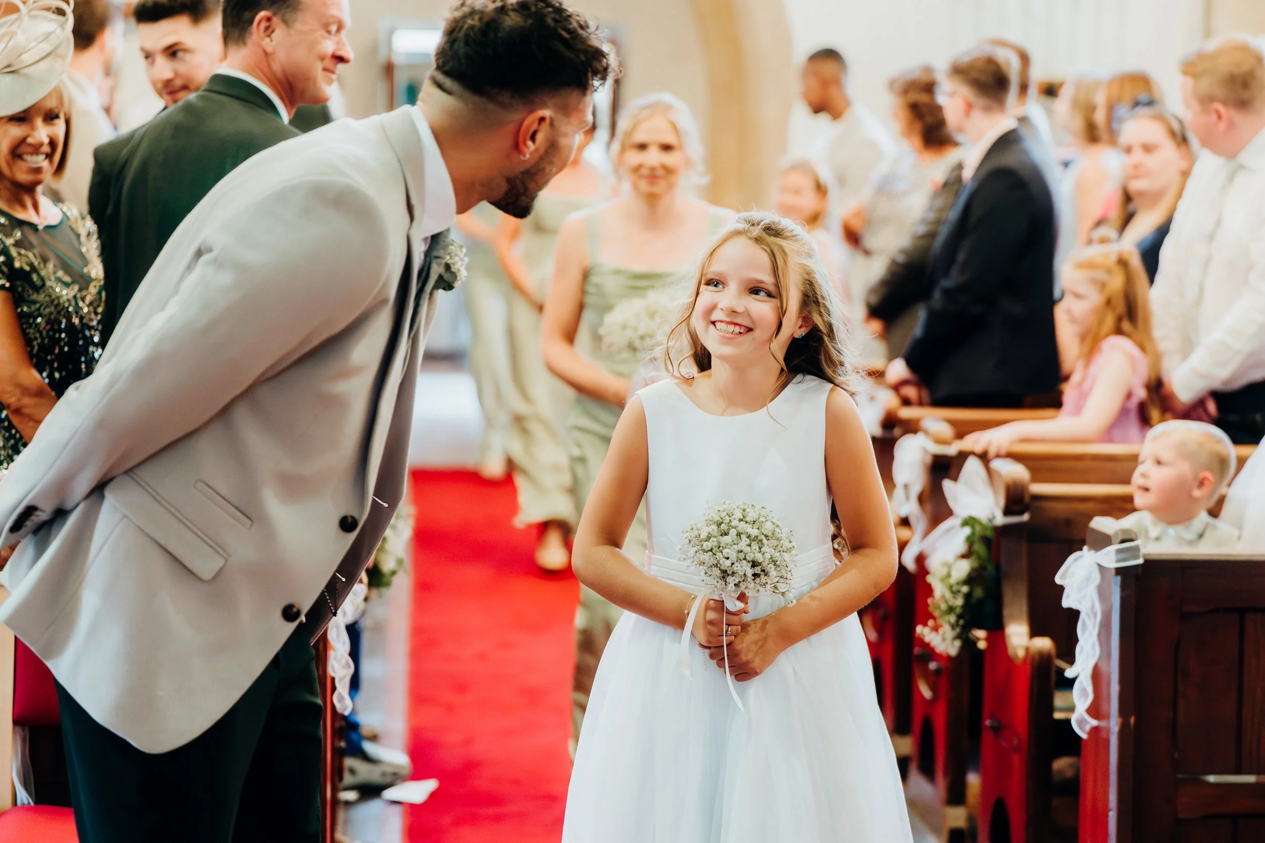Flower girl smiling at groom during wedding ceremony at church near Elstead, Surrey