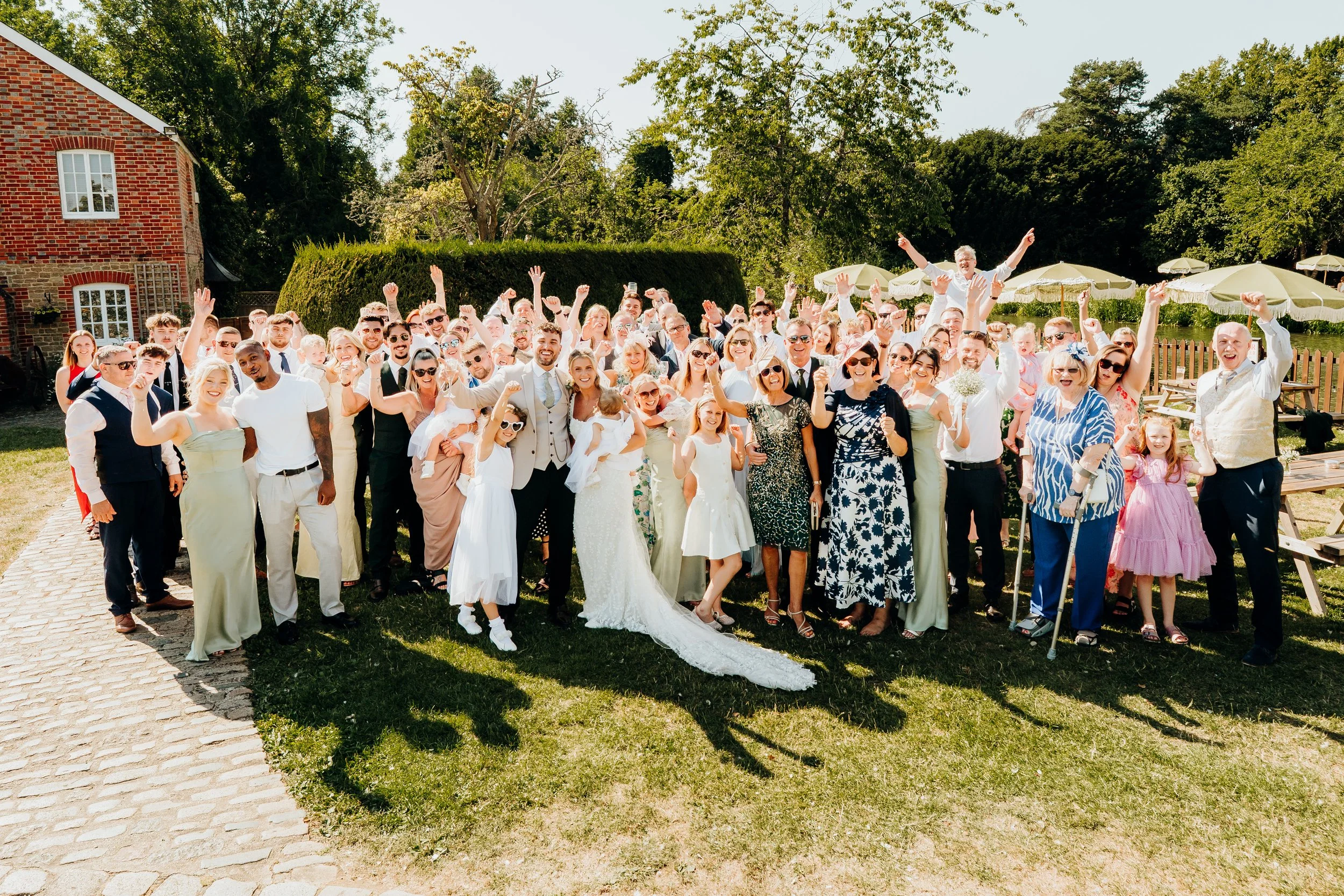 Wedding party group photo cheering outside The Mill at Elstead wedding venue, Surrey