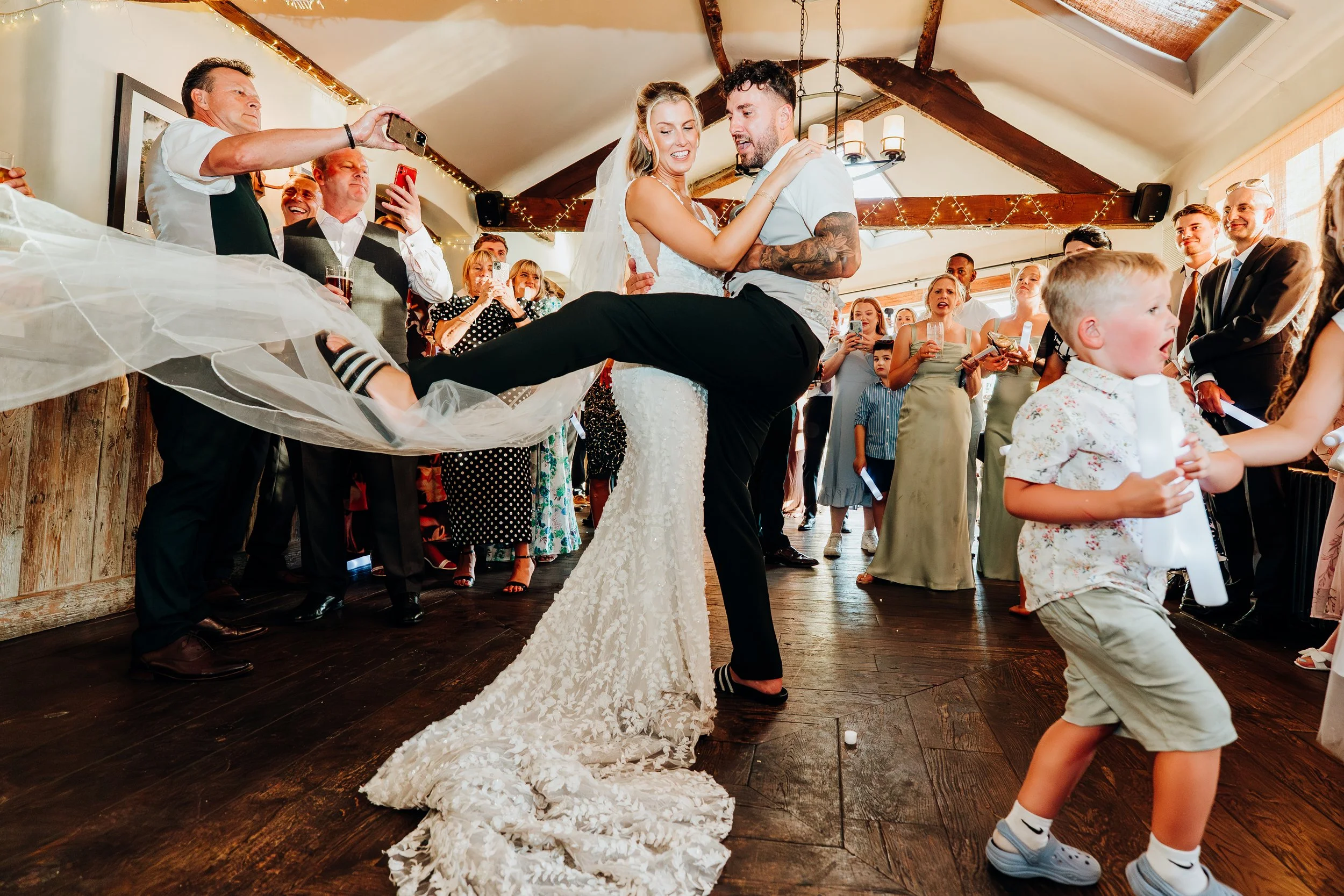 Groom lifting bride while dancing with guests at The Mill at Elstead wedding reception, Surrey