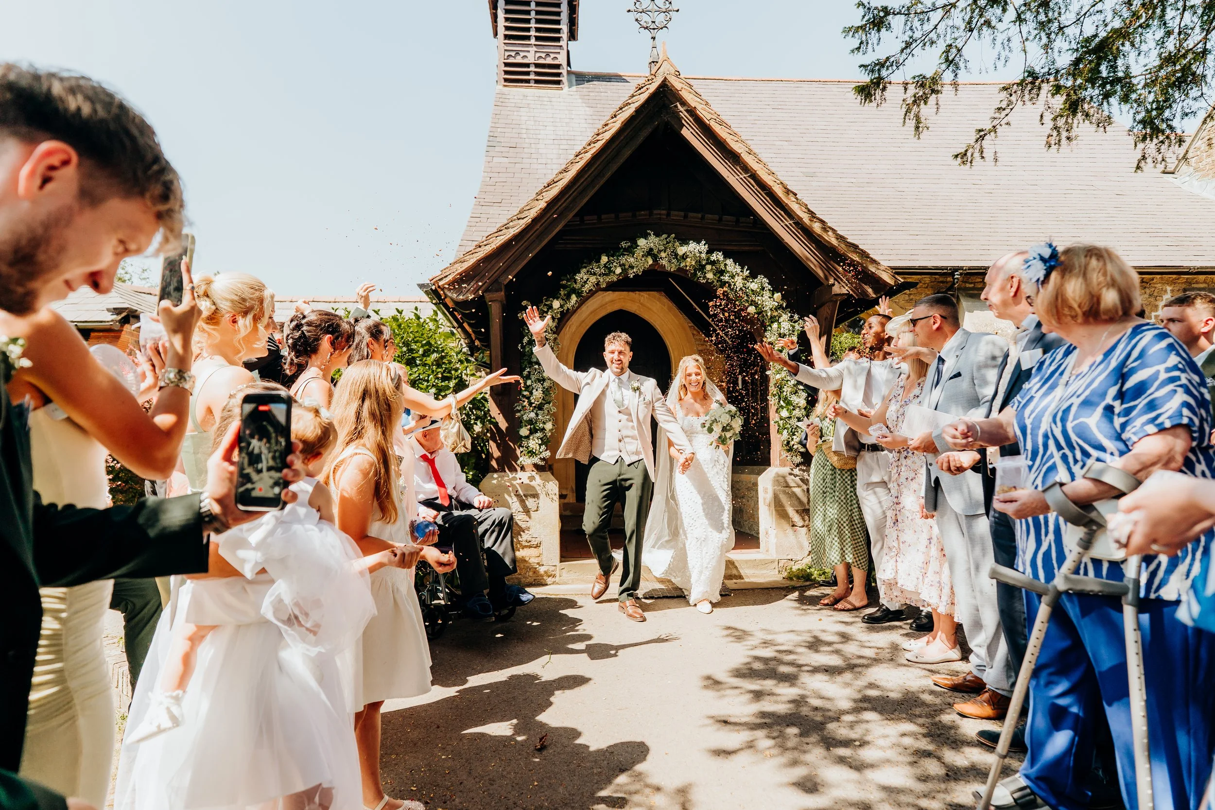 Bride and groom exiting through confetti at the church porch after their wedding ceremony, Surrey