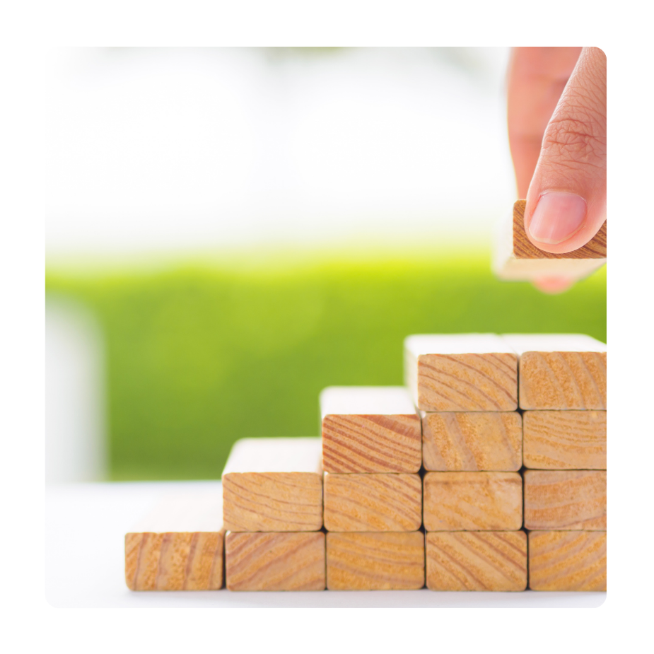 A person stacking wooden blocks in ascending order with a blurred green background.