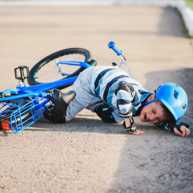 A young boy in a blue helmet and striped shirt lying on the ground next to his fallen blue bicycle, appearing to be hurt or upset.
