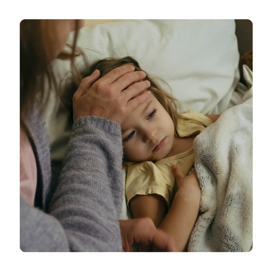 A young girl lying in bed with a mother gently holding her head, showing concern or care.