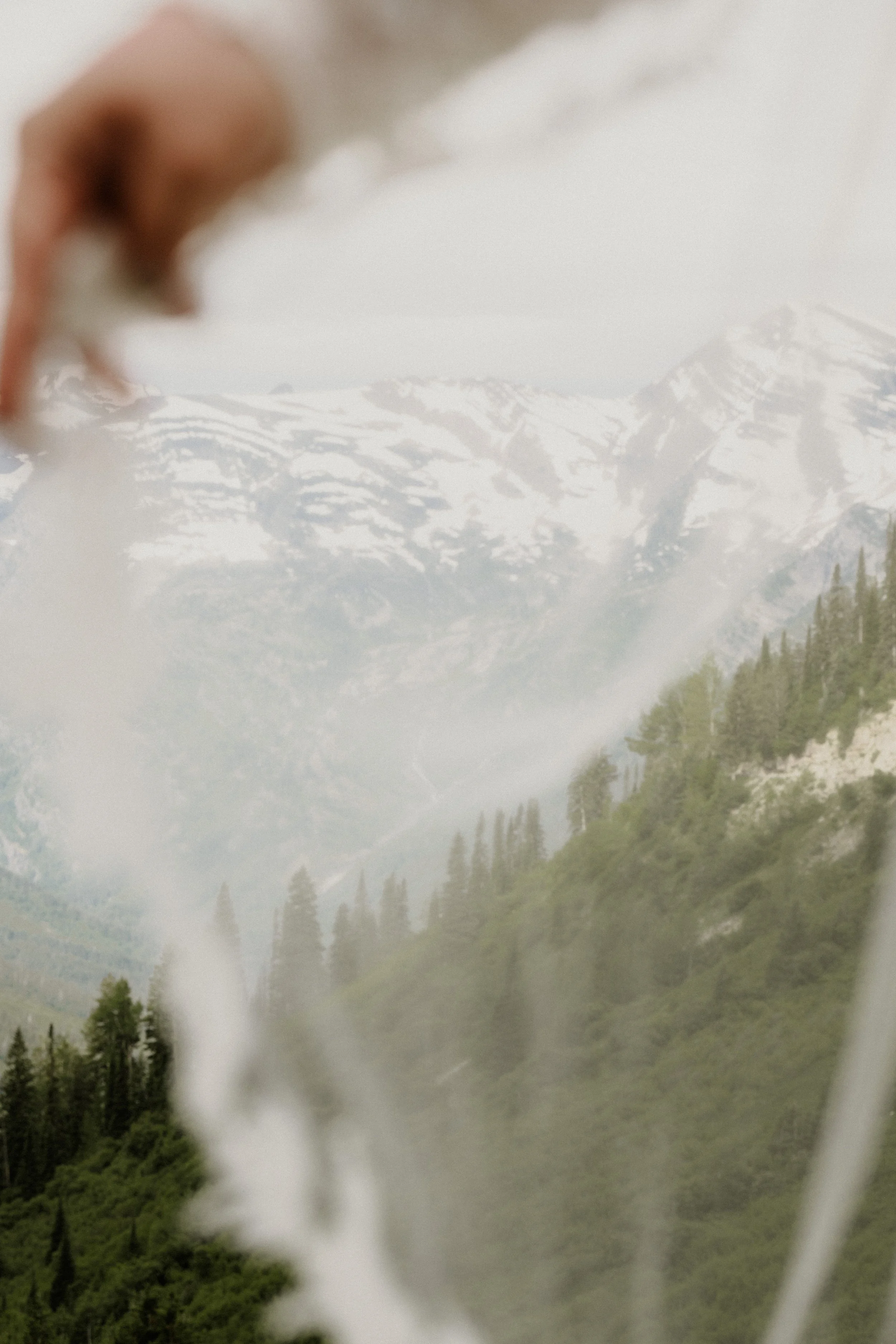 Blurred image of a mountain range with snow-covered peaks, surrounded by green forests and a waterfall in the foreground.