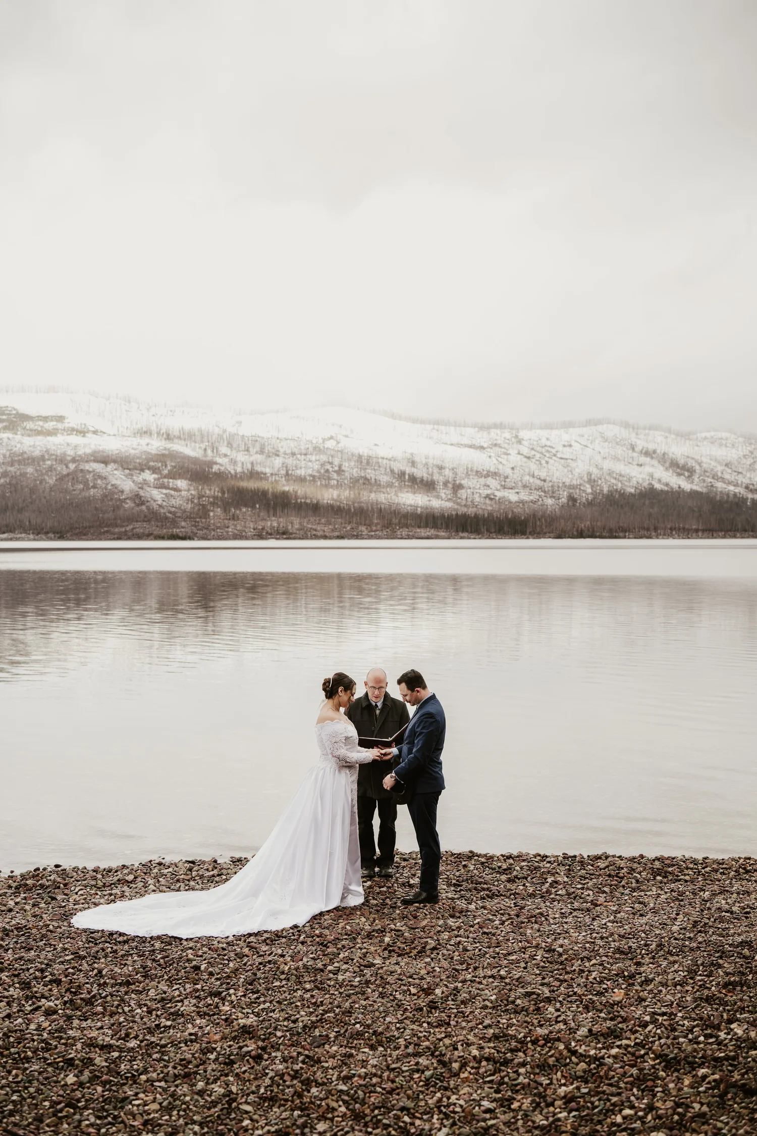 Bride and groom exchanging vows beside a calm lake with snowy mountains behind