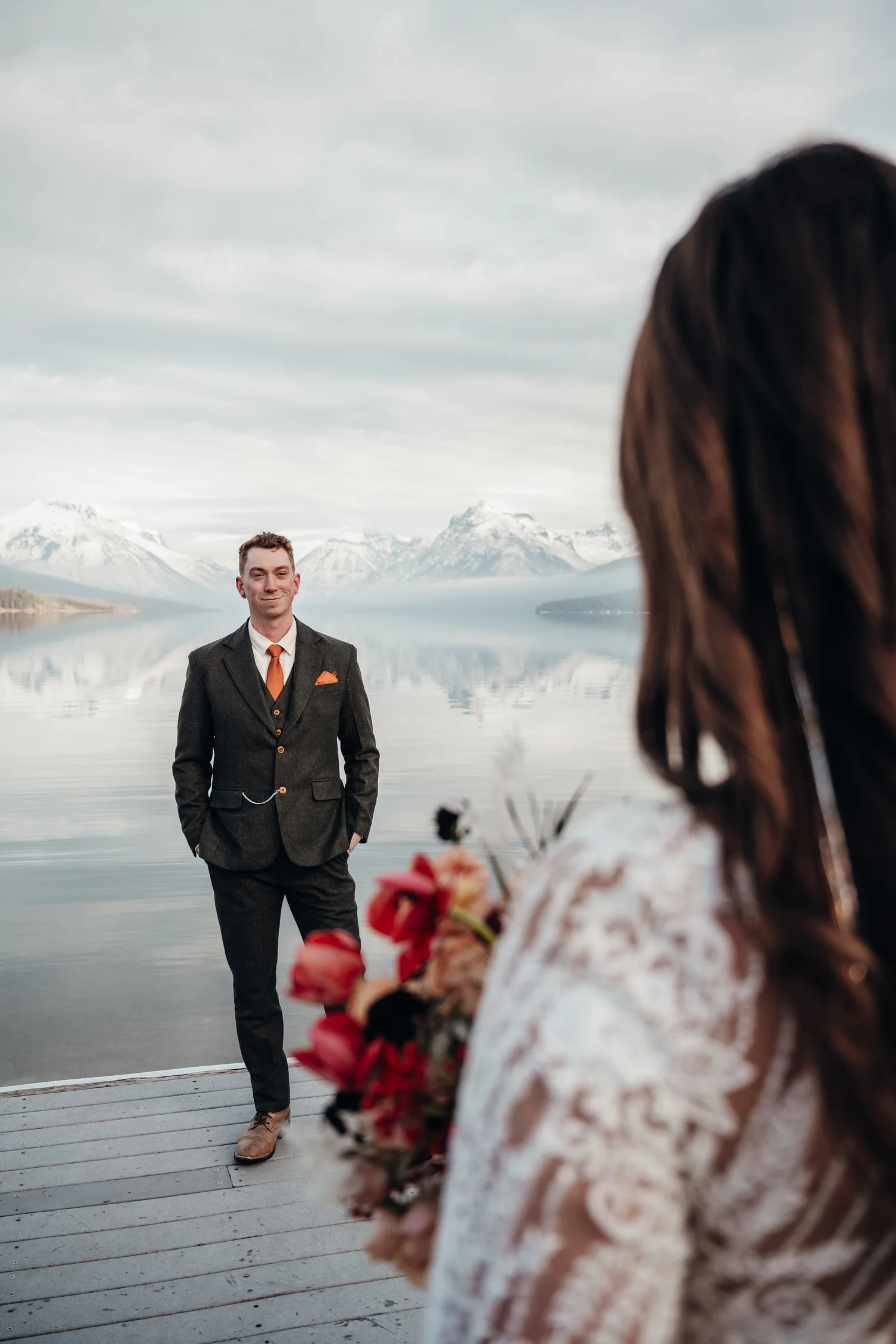 Newlyweds on the dock at Lake McDonald, the groom in a suit with an orange tie and the bride holding her bouquet