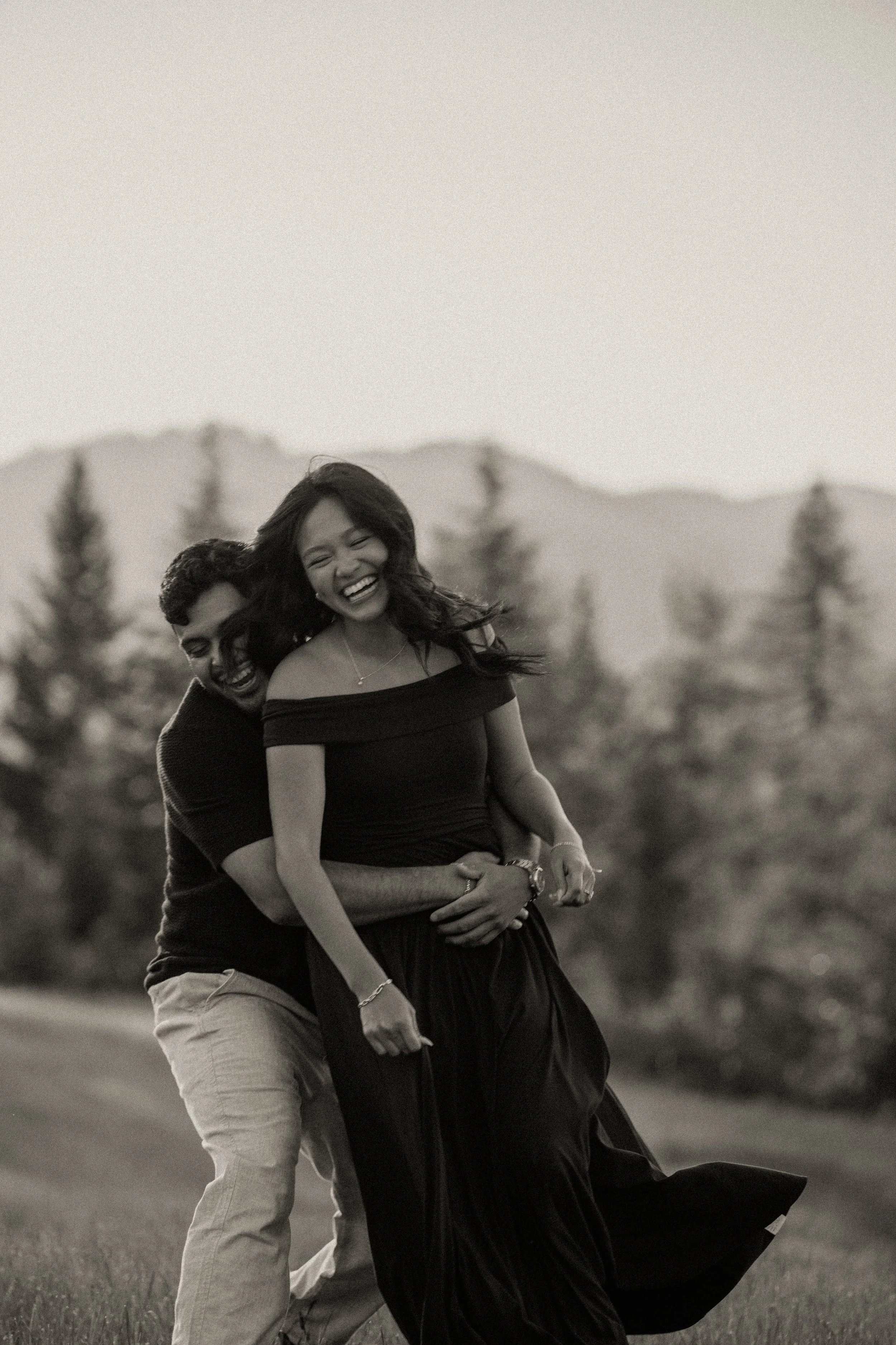 Black and white photo of a couple laughing and hugging in a Glacier National Park field