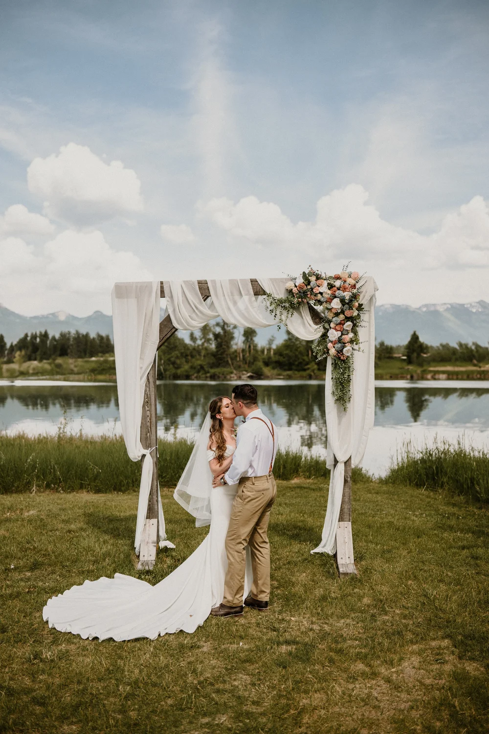 Couple kissing under a floral arch beside a lake in Montana