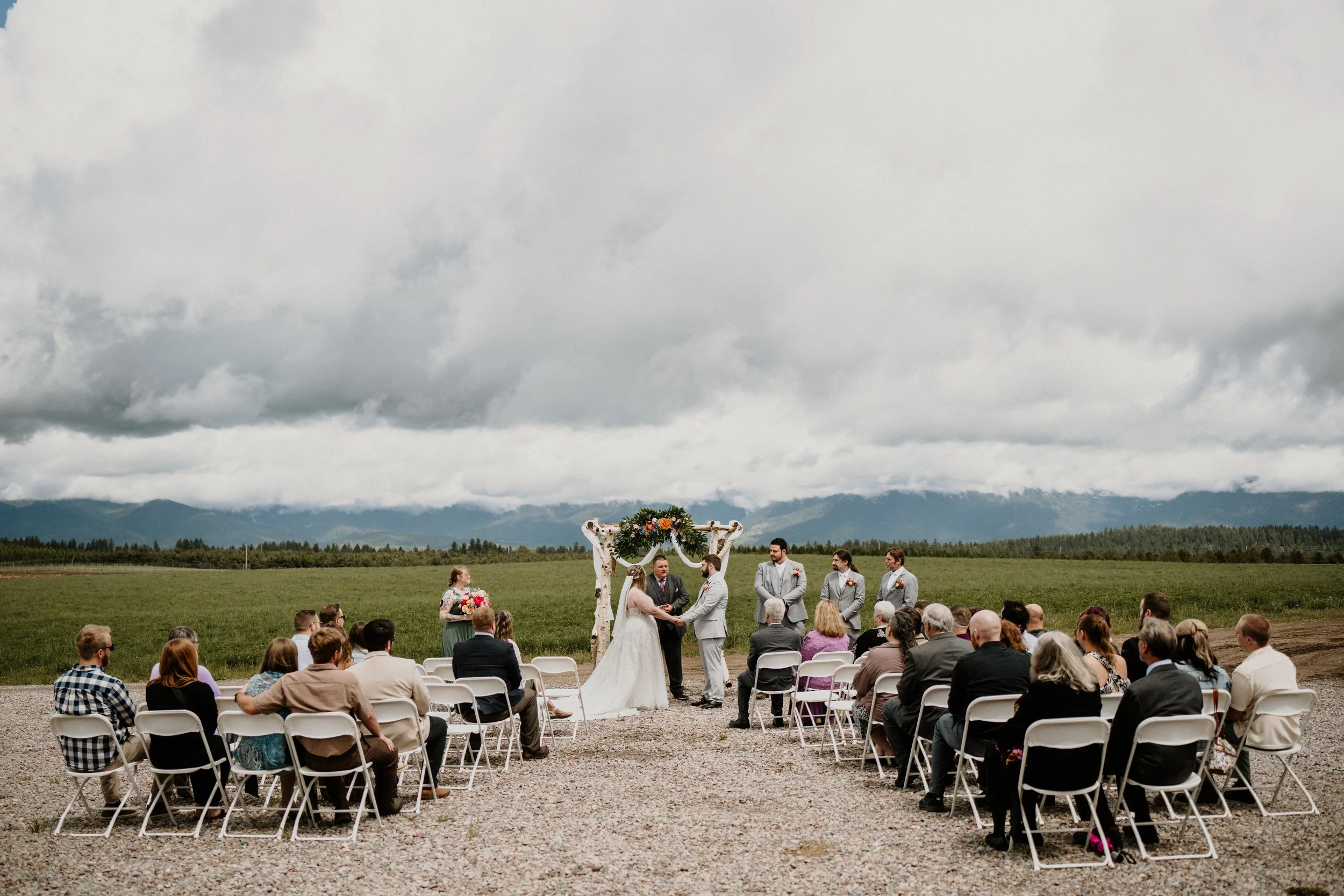 Alex and Lily exchange vows under a decorated arch at their Montana wedding, with mountains in the distance.