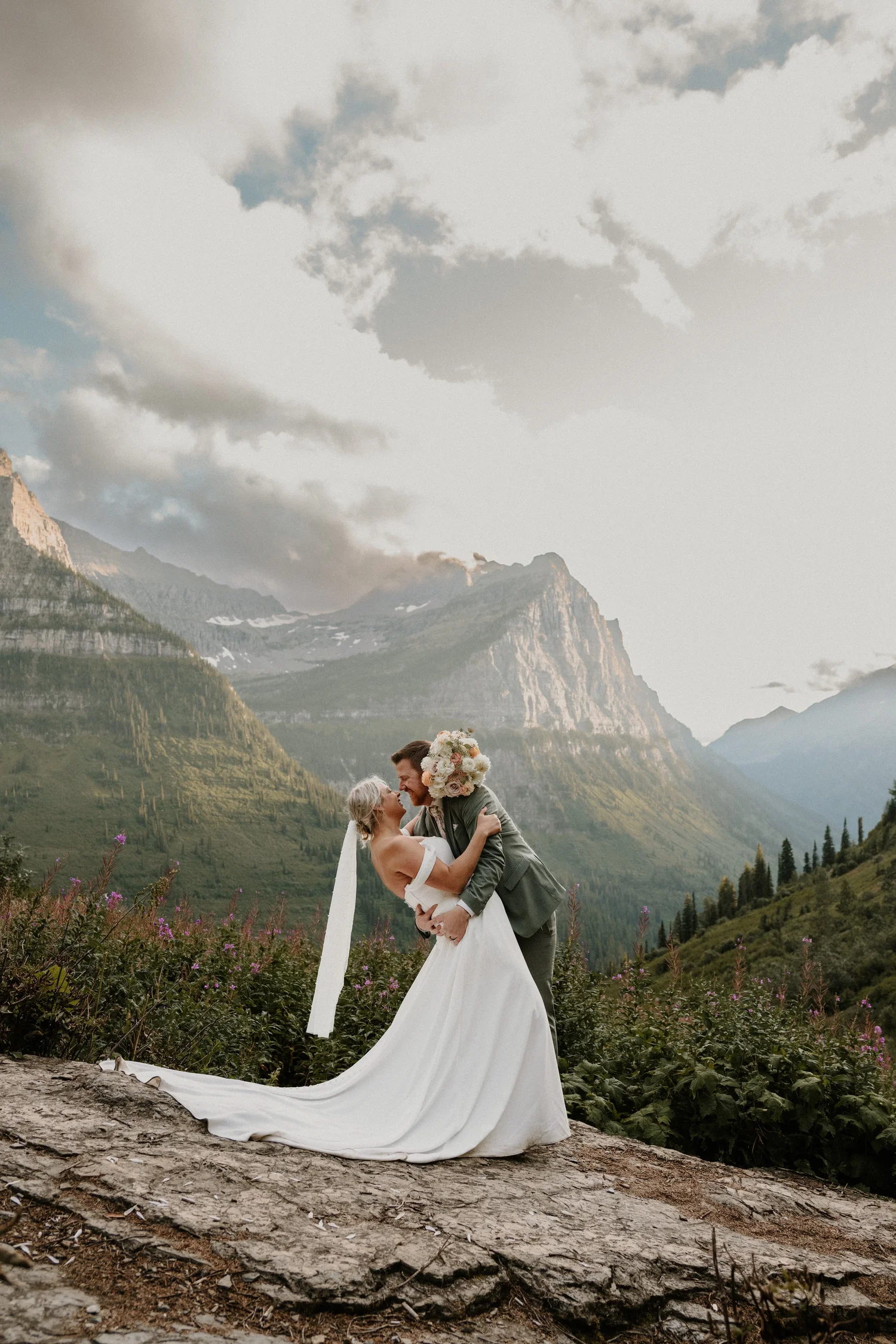 Bride and groom embracing on green slopes beneath rocky peaks
