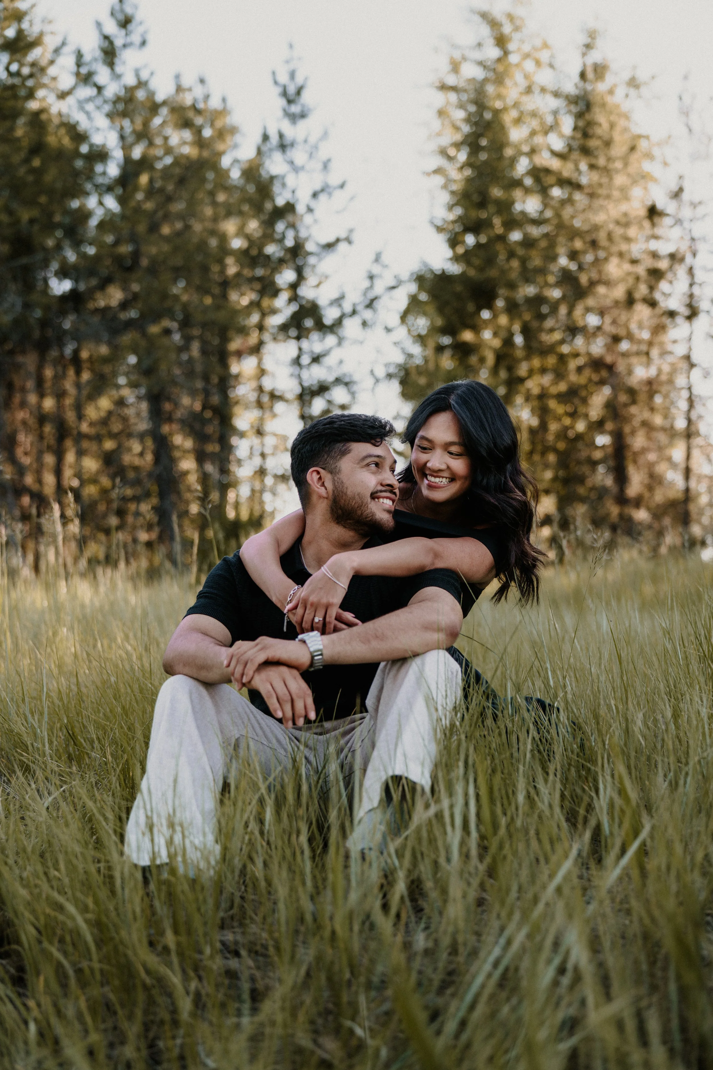 Engaged couple sitting close in a grassy field in Glacier National Park