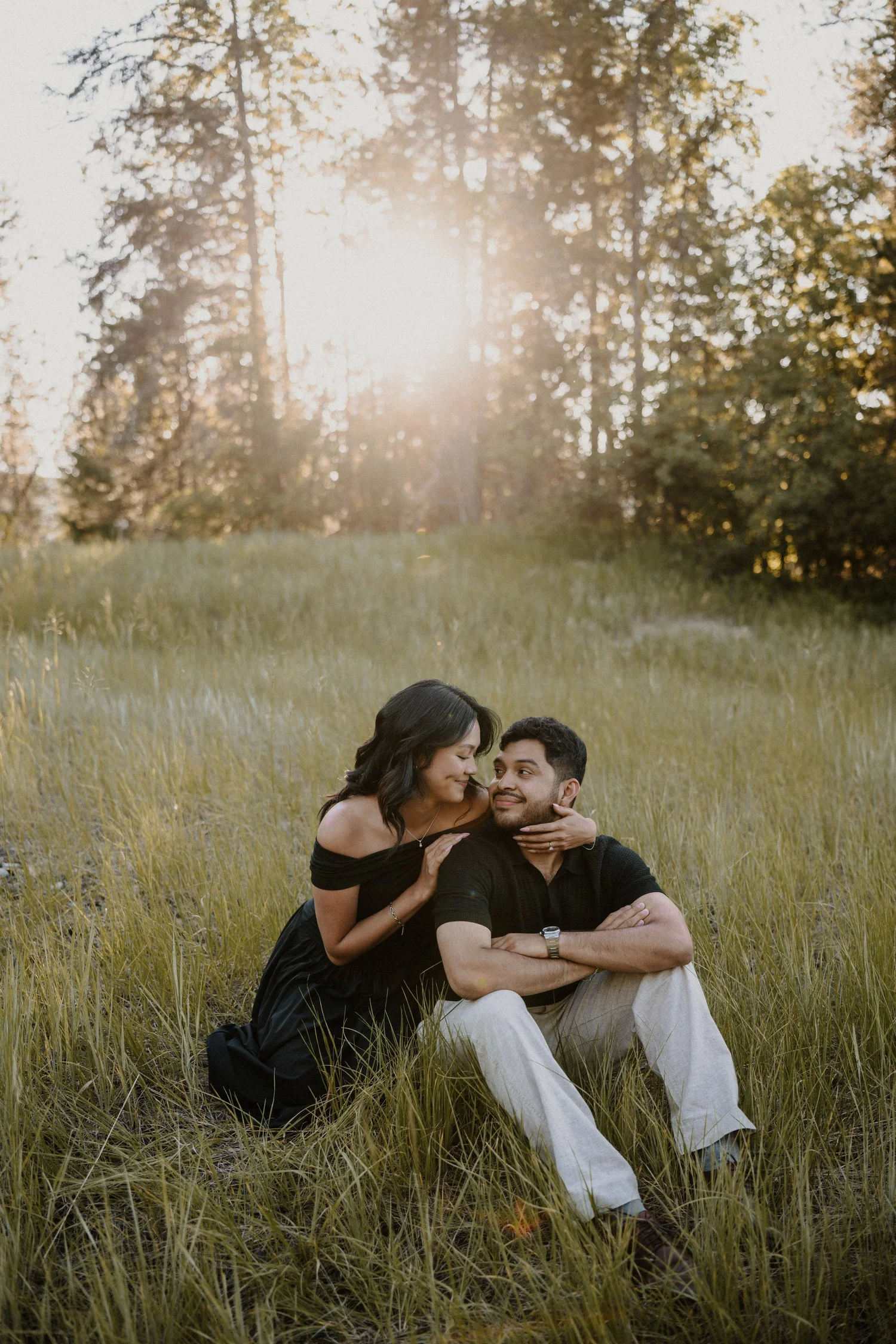 Couple sitting in a grassy field at sunset gazing at each other in Glacier National Park