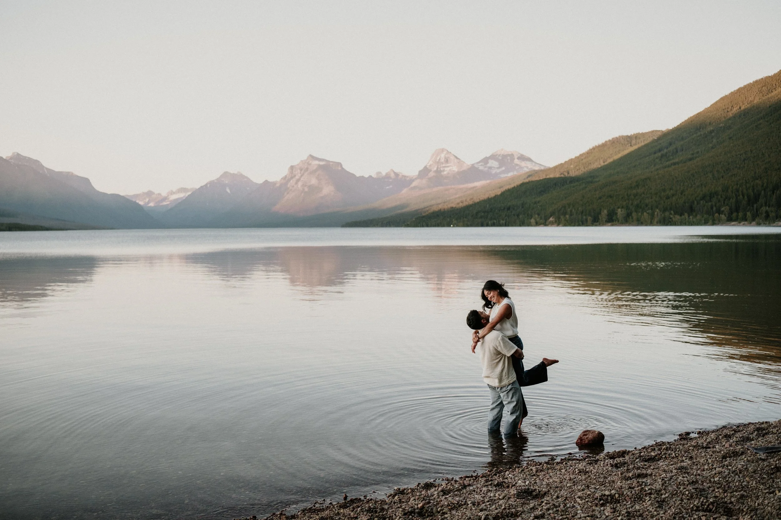 Newly engaged couple embracing in a Glacier National Park lake at sunset