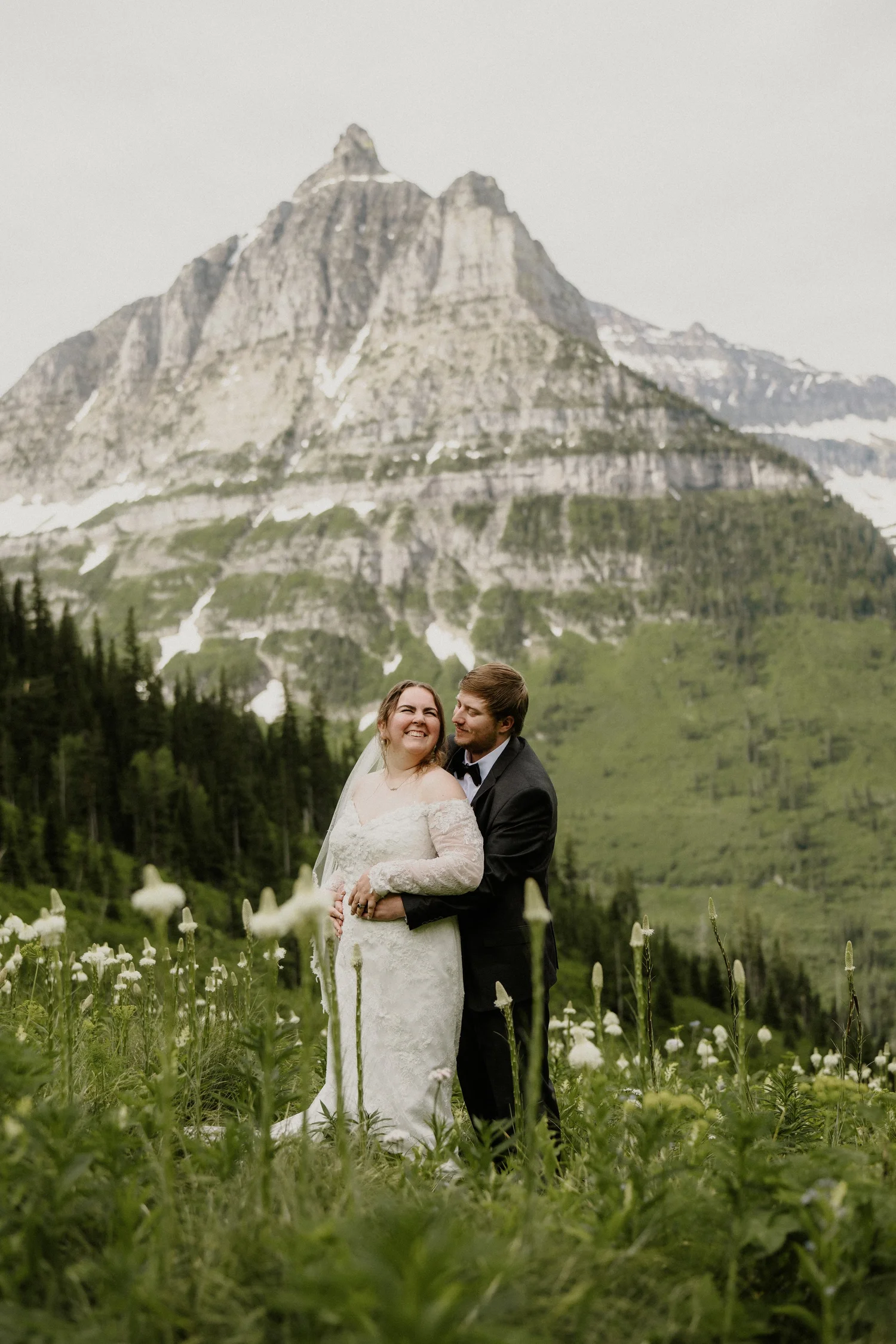 Newlyweds in a field of white flowers with a mountain range behind