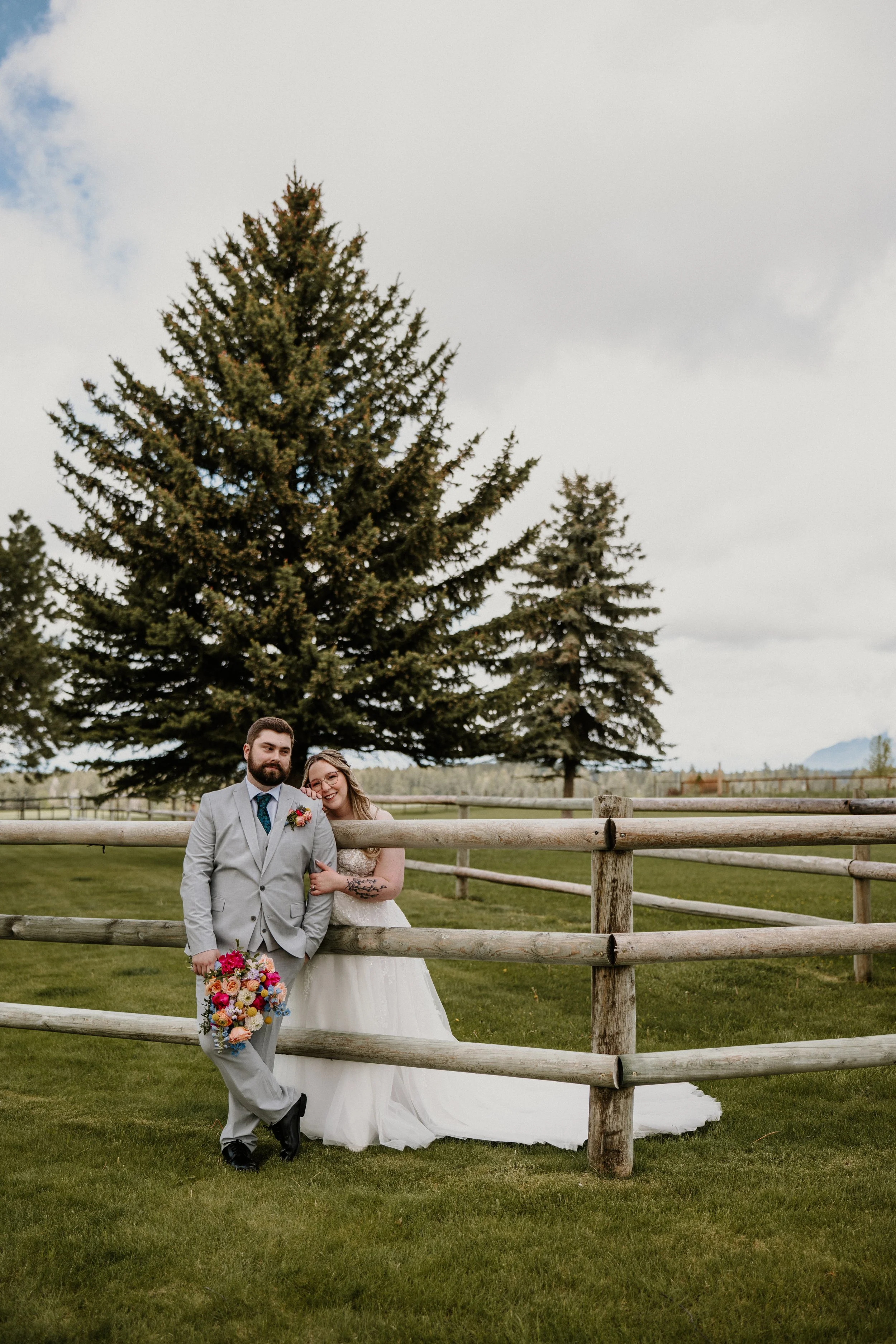 Alex and Lily near a wooden fence with evergreens behind them on a cloudy Montana afternoon.
