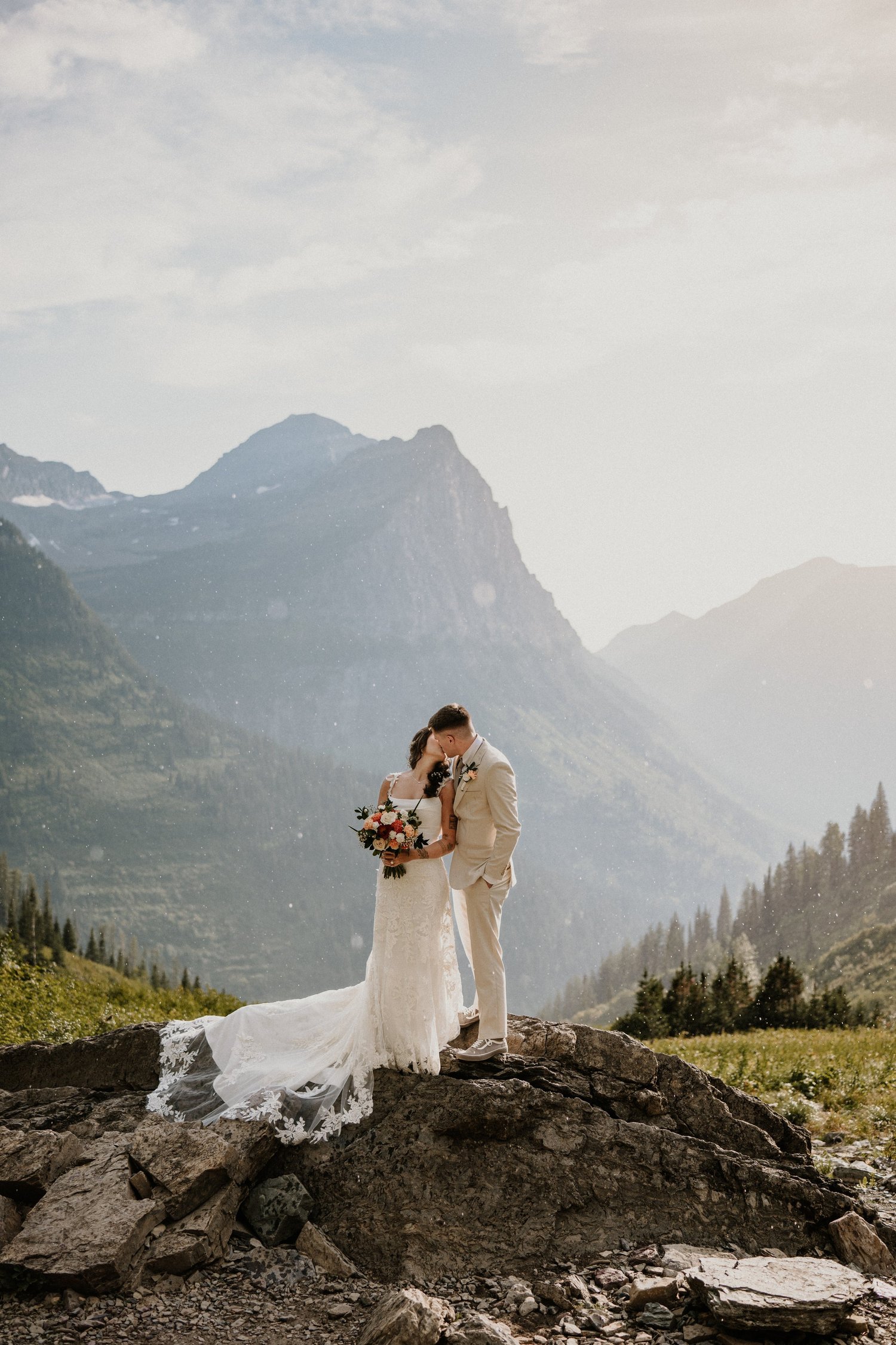Bride and groom kiss on a rocky ledge surrounded by mountains