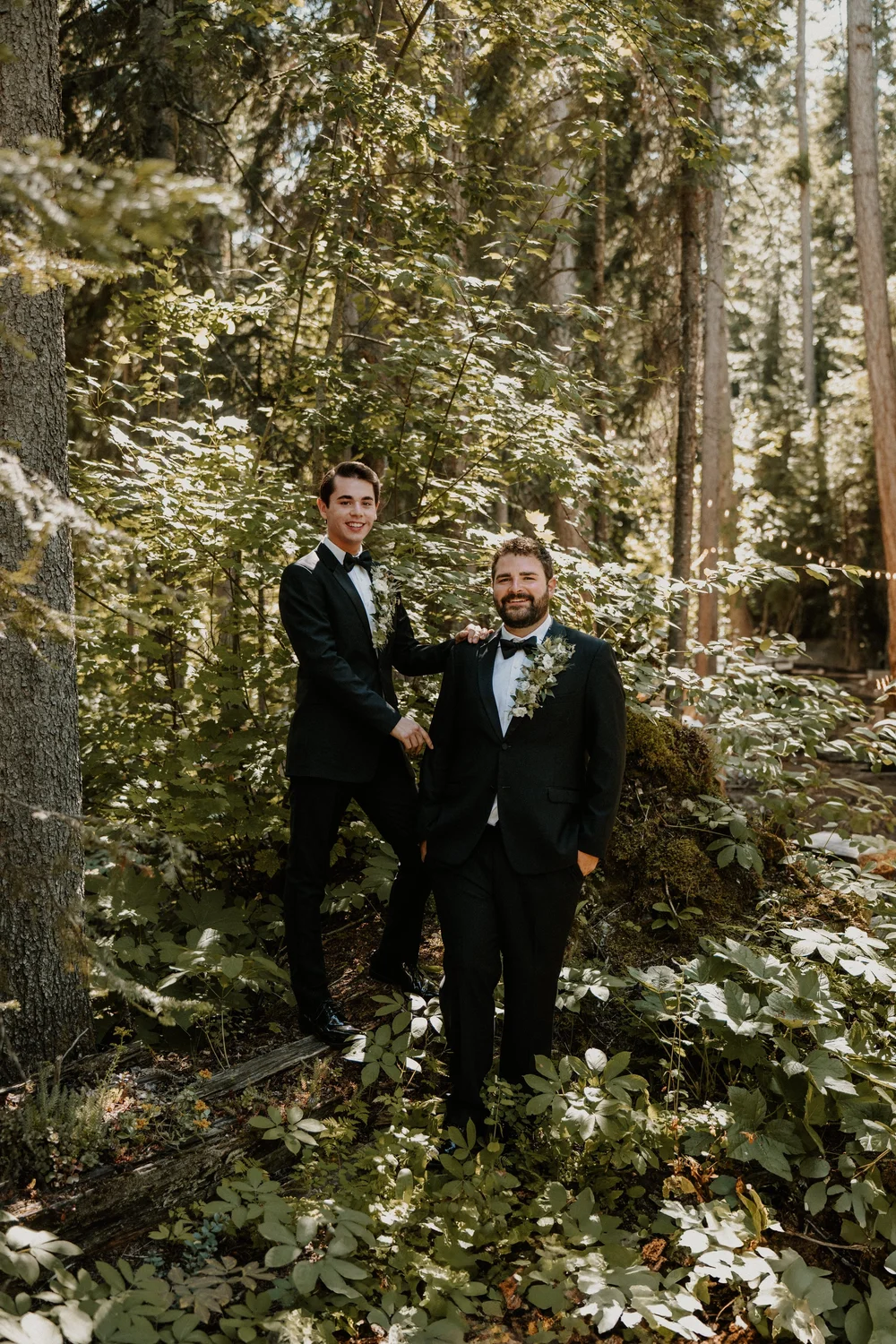 Two grooms in tuxedos in a Montana forest on their wedding day