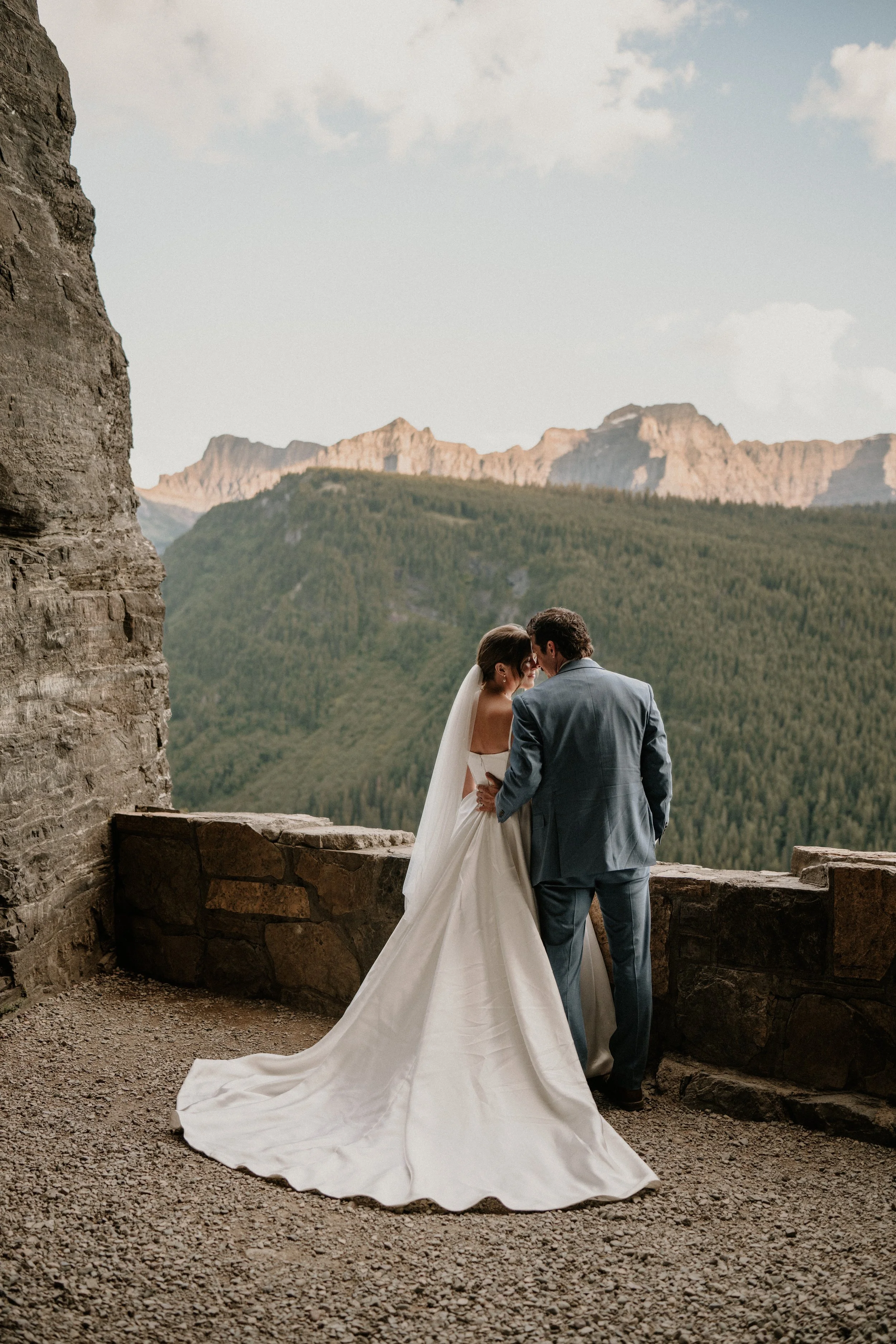 A bride and groom standing close together on a stone balcony with a mountain landscape in the background.