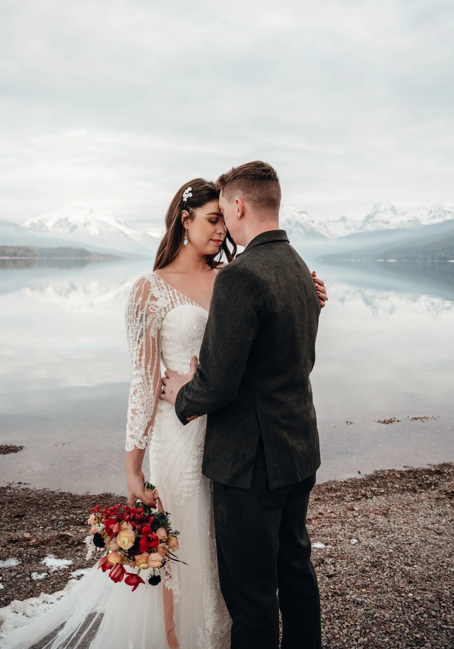 Bride and groom embracing on the lakeshore during their winter session in Glacier National Park