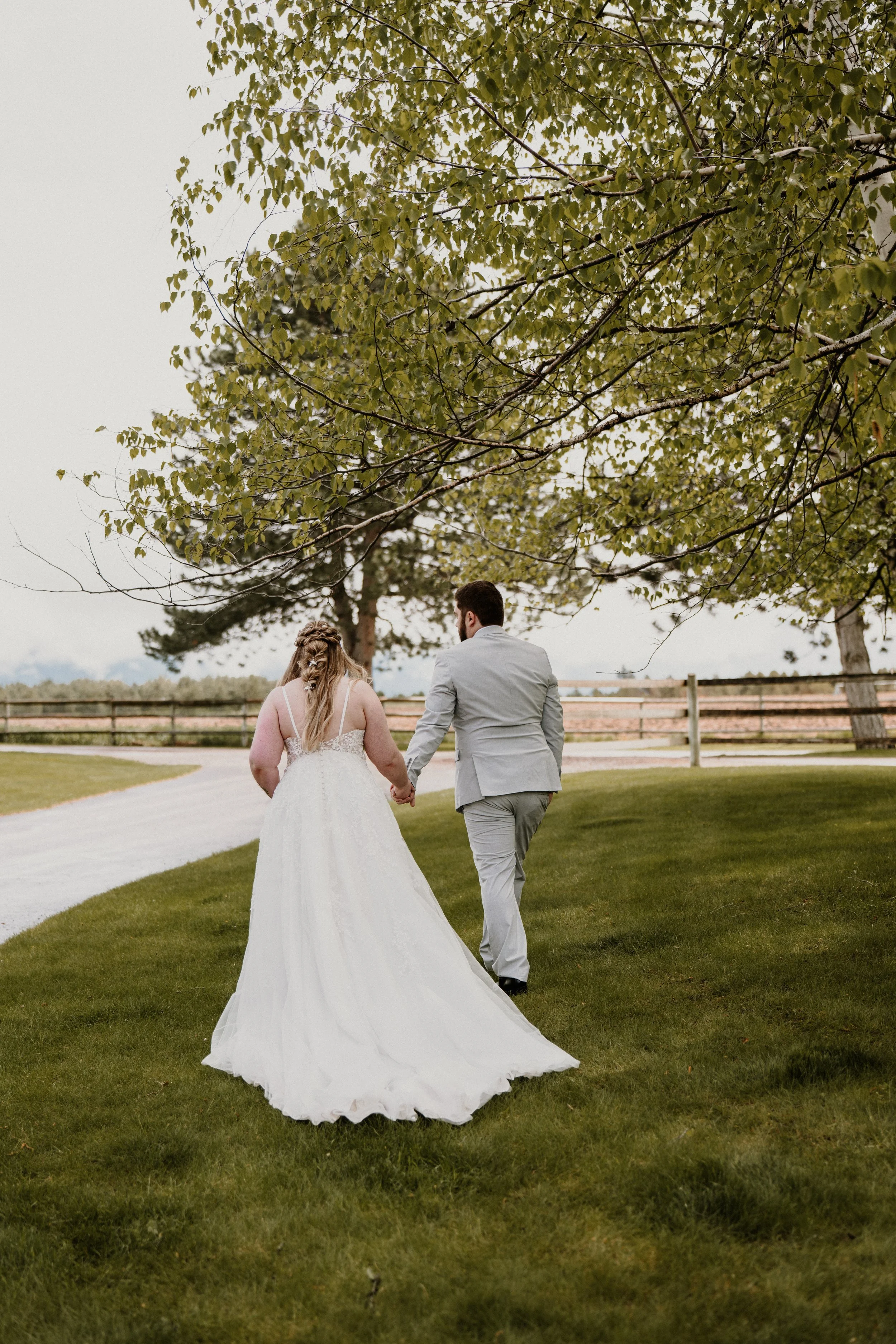 The couple walks hand in hand along a grassy path on a cloudy Montana day.