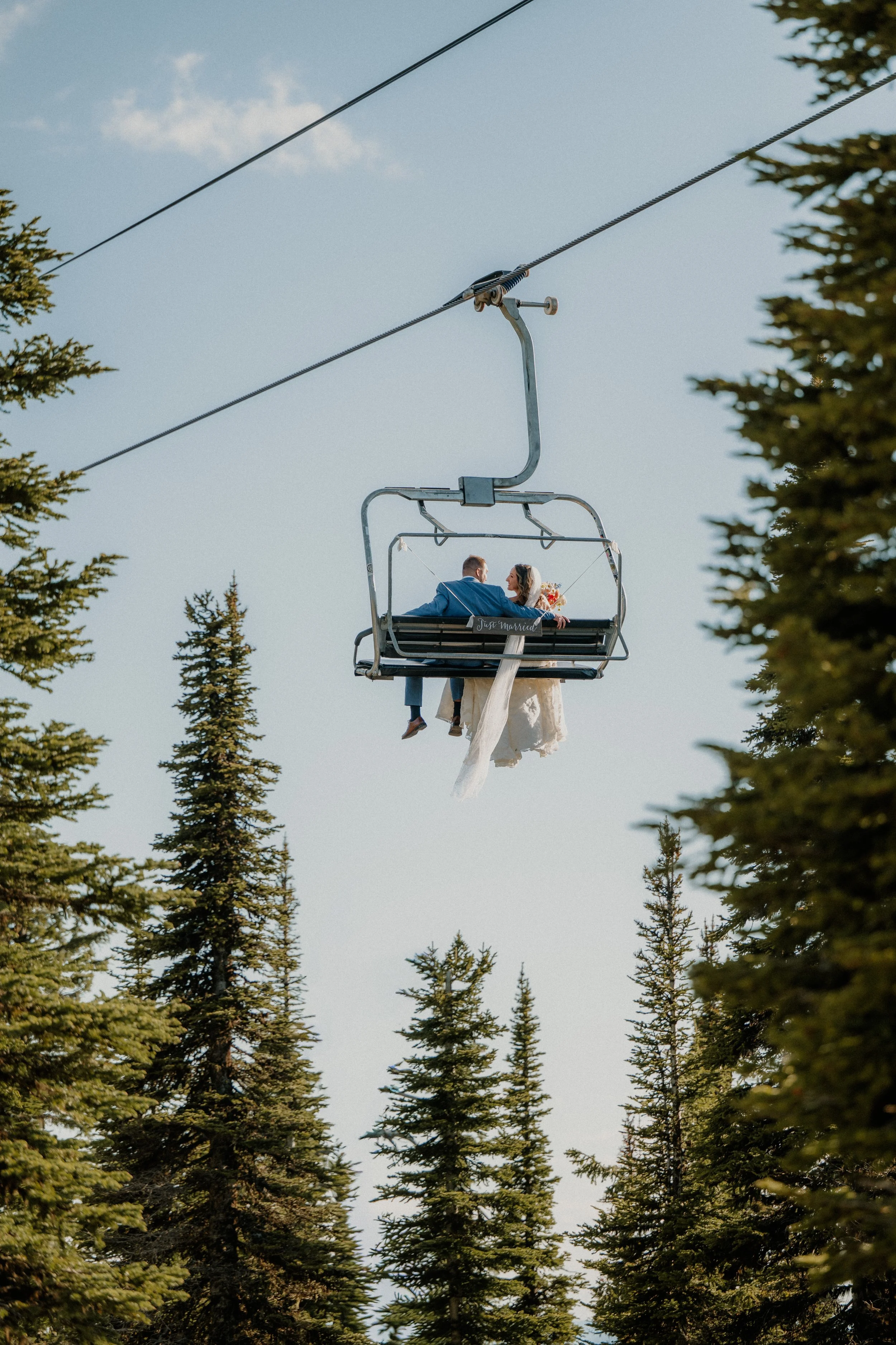 Just married couple on a chairlift among pine trees, Montana elopement