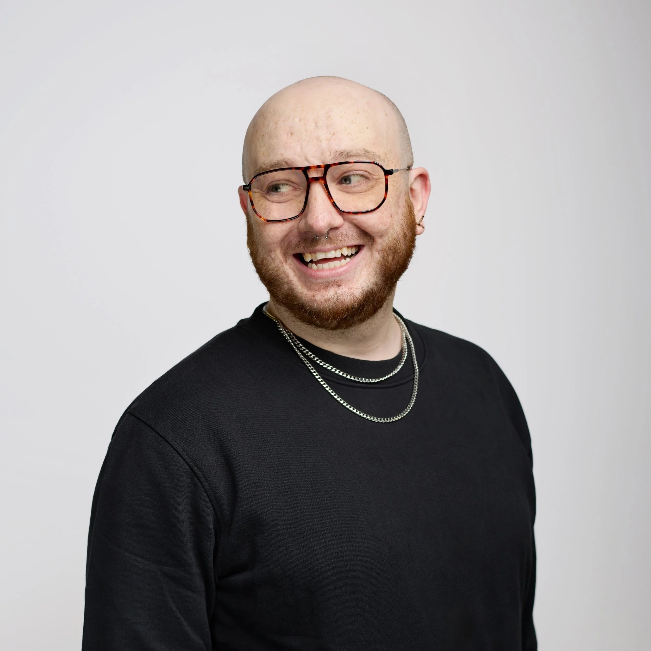 Portrait of a young man with dark hair wearing sunglasses and a black hoodie against a black background.