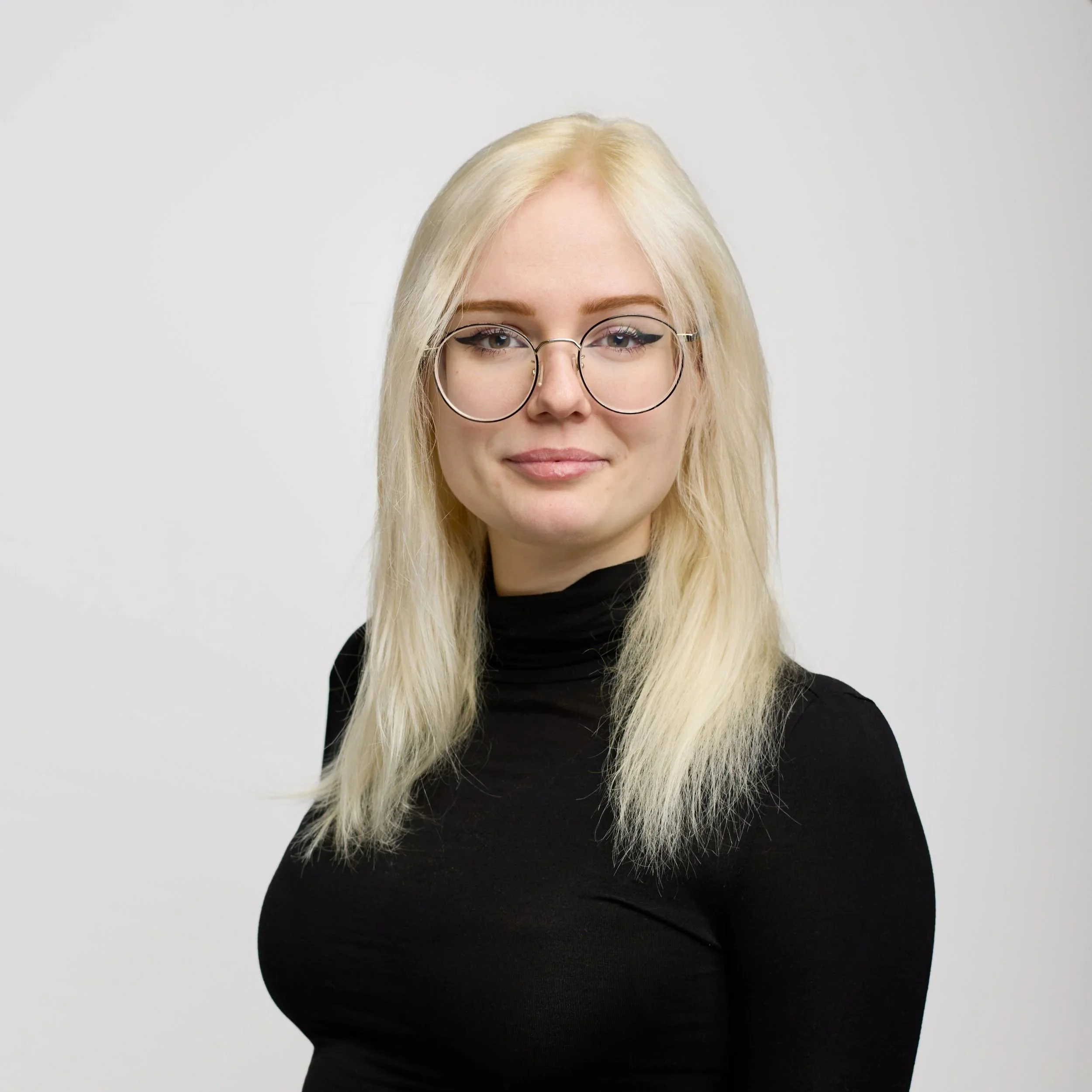 A young woman with medium length bleach blonde hair, glasses,  black turtle neck, on a white background.