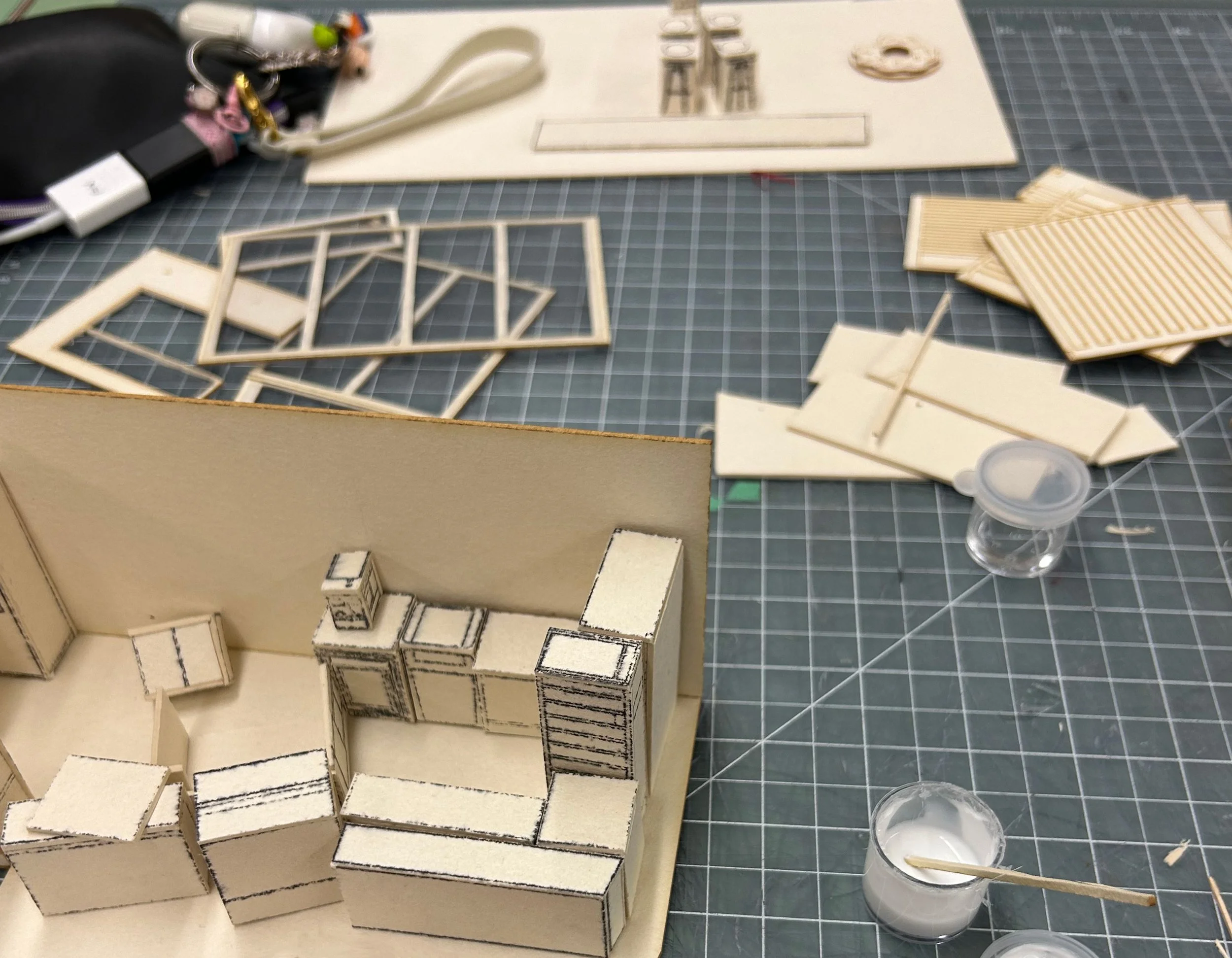 Miniature furniture pieces for a dollhouse, including a cabinet, dresser, and small shelves, placed on a cutting mat.