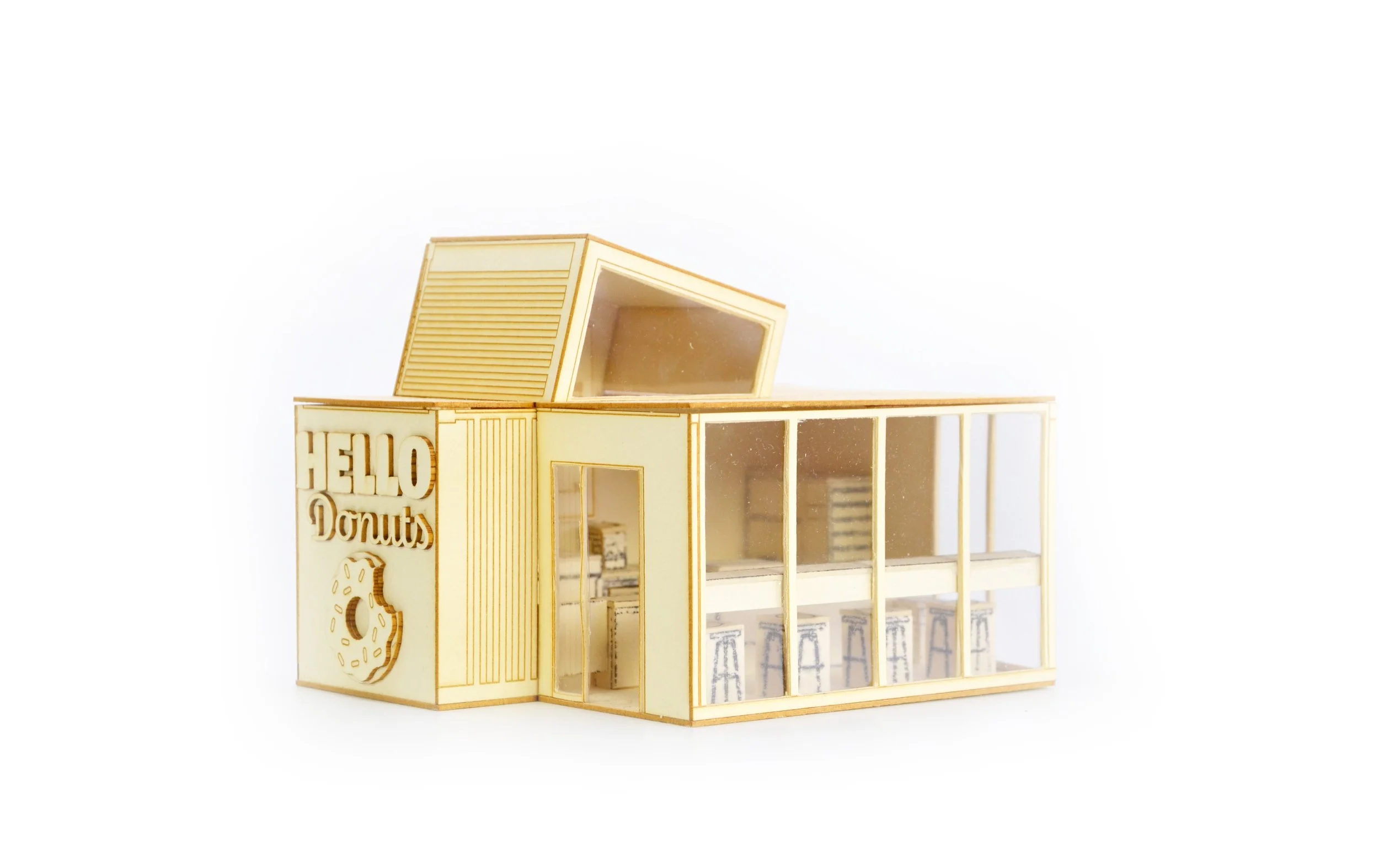 Miniature wooden model of a donut shop with the sign "HELLO Donuts" and large windows, designed for a diorama or model display.
