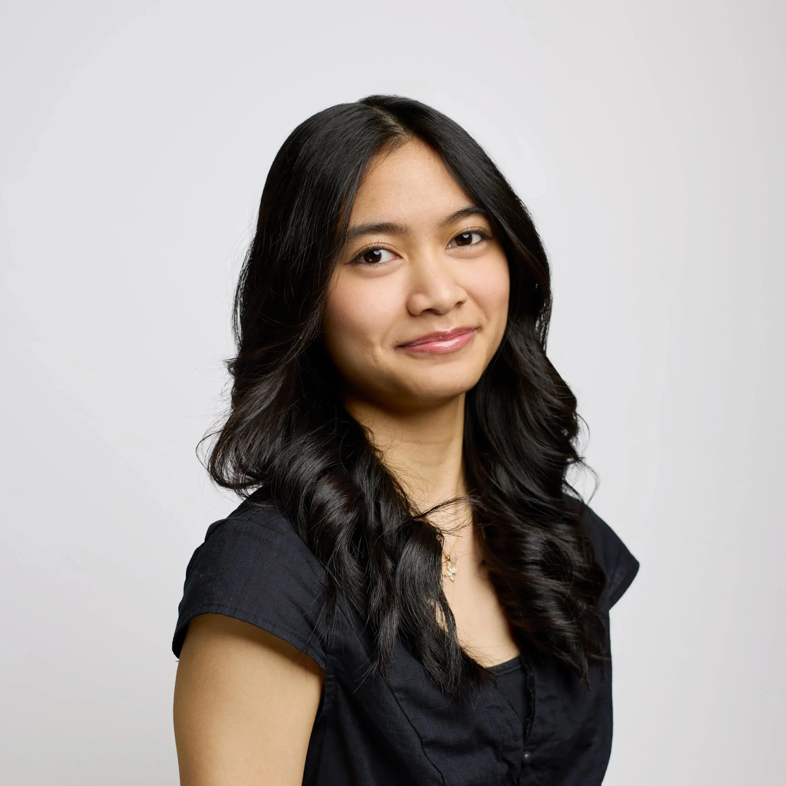 Young lady with dark brown hair, shoulder length, smiling at the camera