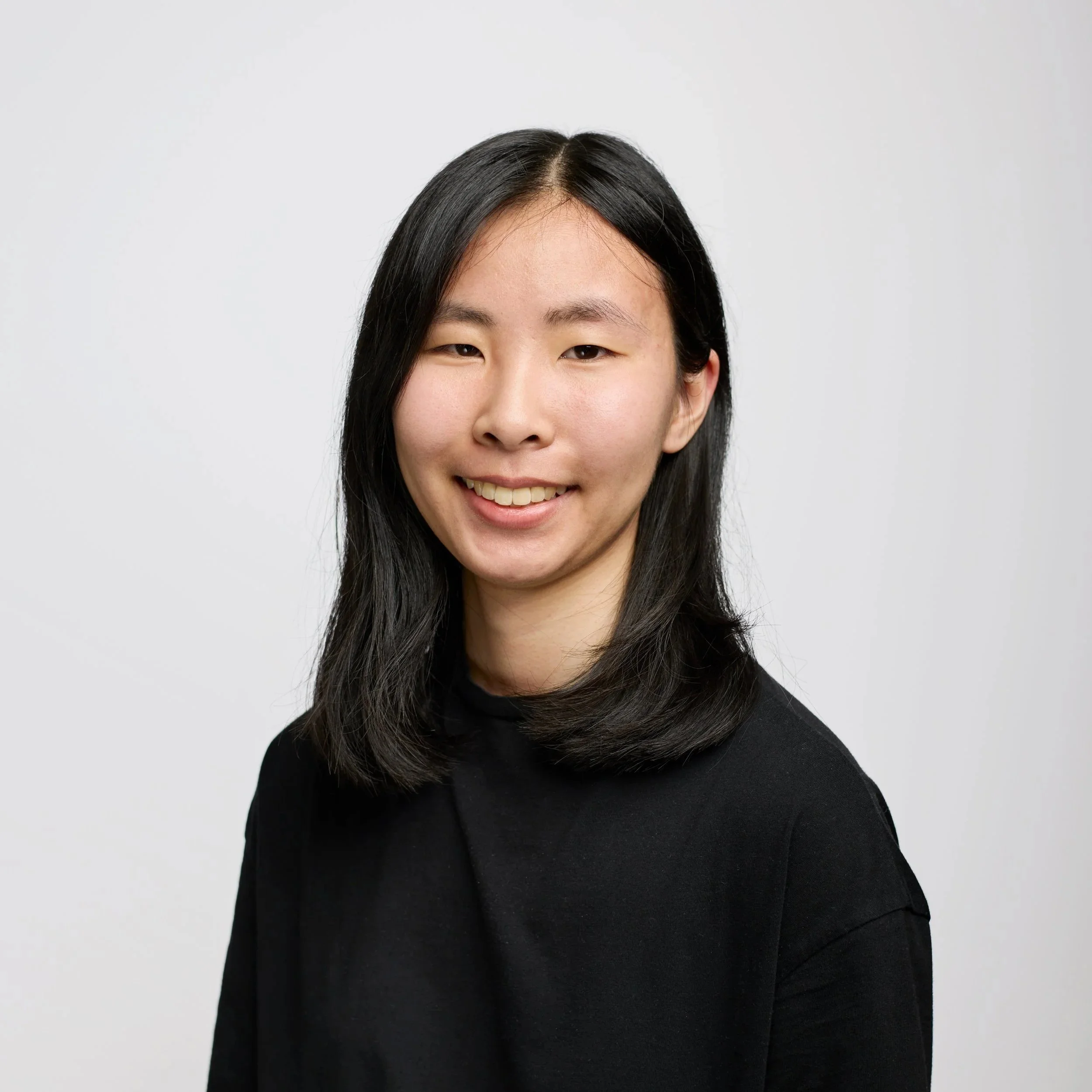 A young woman with short black hair, wearing a black long sleeve, on a white background.