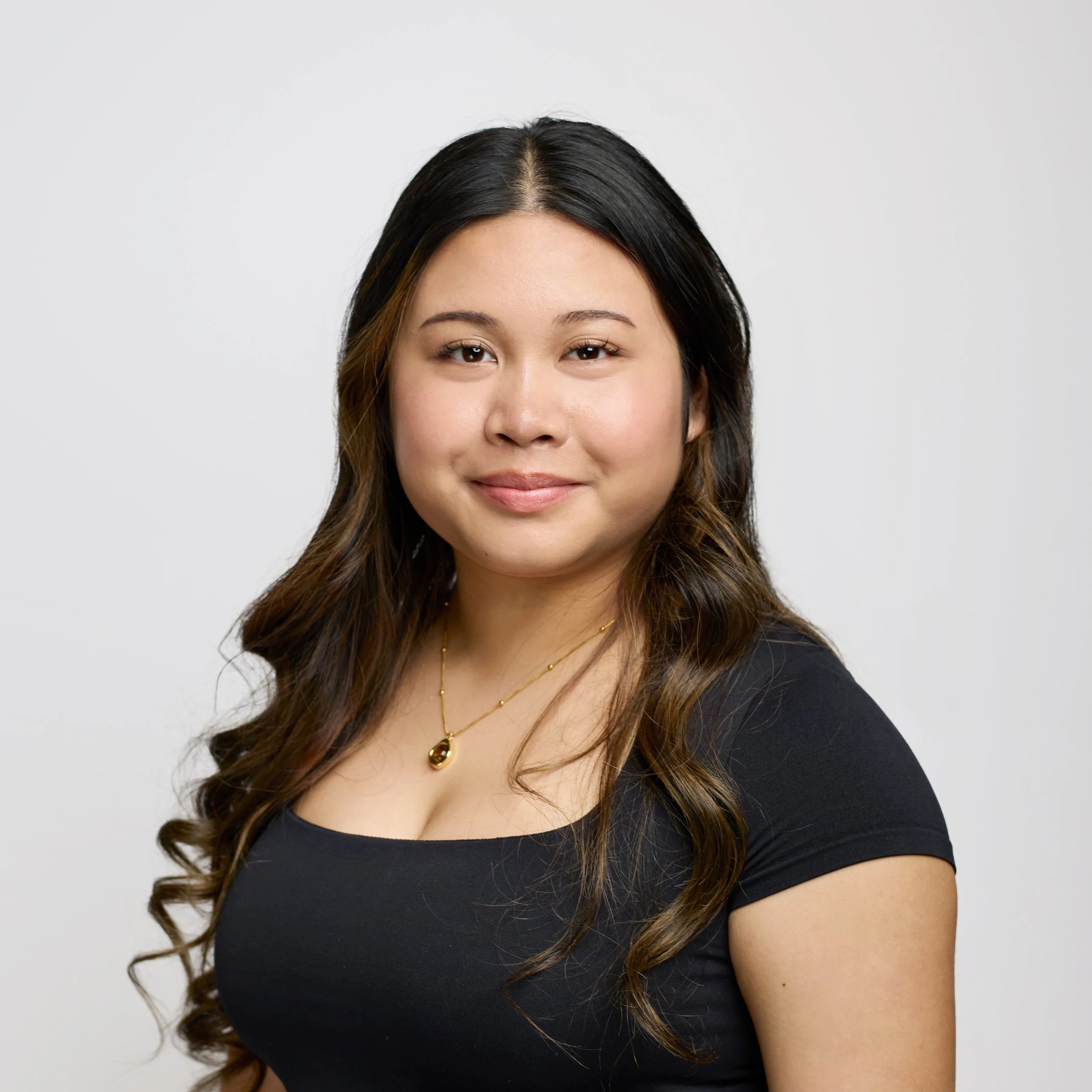 A young woman with long brown hair, wearing a black top and silver jewelry, smiling against a black background.
