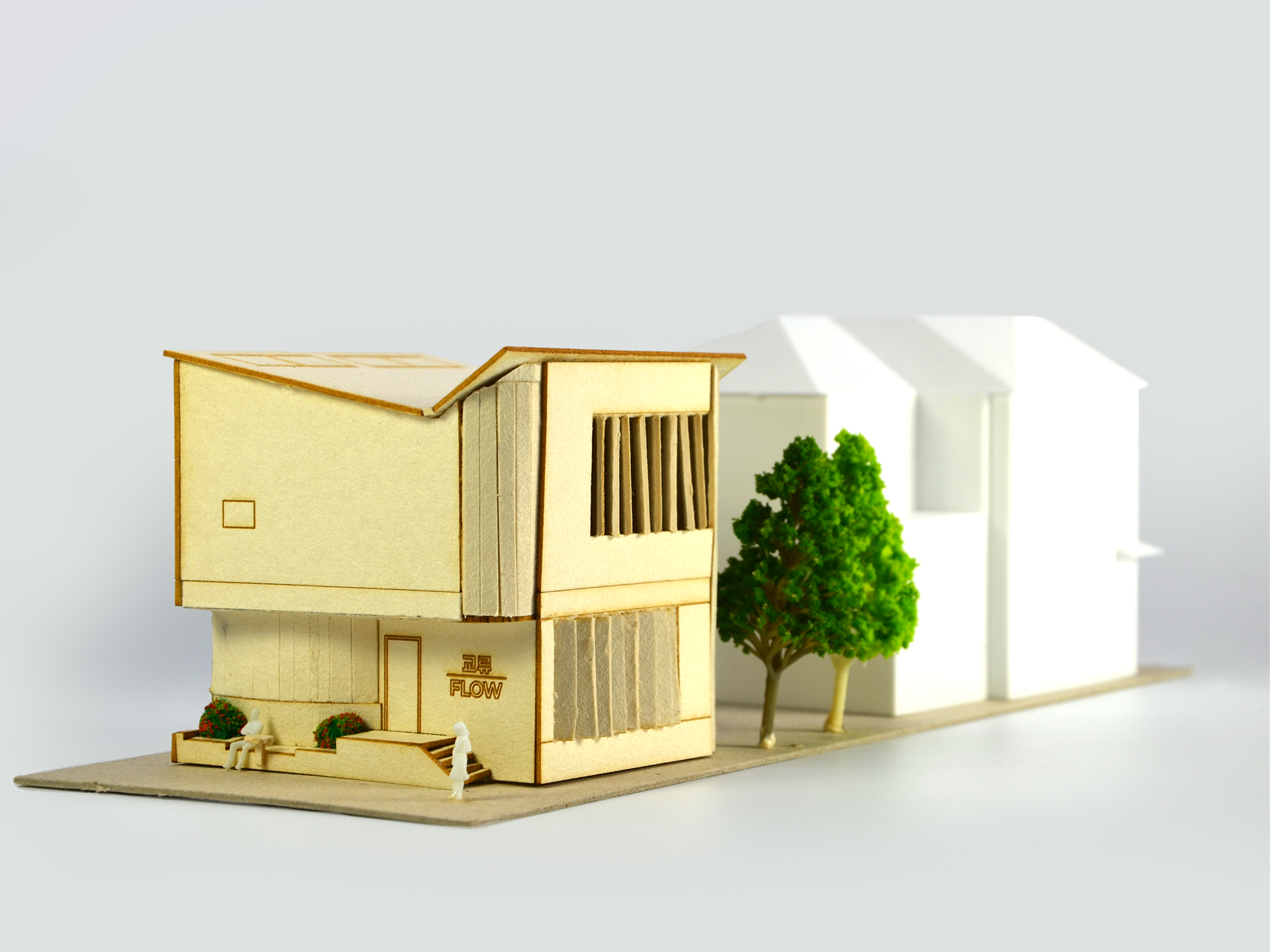 Architectural model of a modern house with trees and miniature people, made of cardboard and paper.