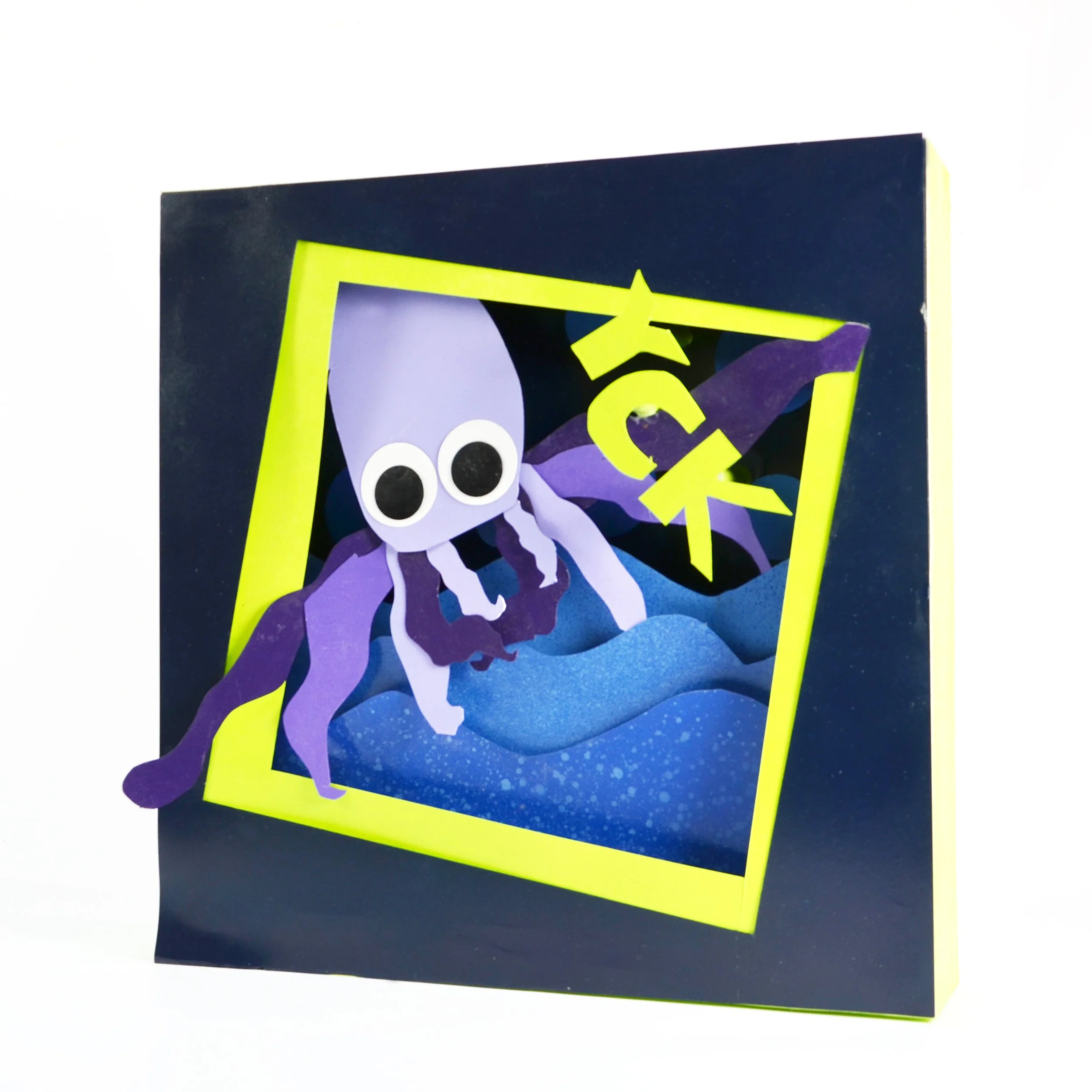 Close-up of a colorful handmade paper craft featuring a purple and white owl with googly eyes, set against a black and yellow background.