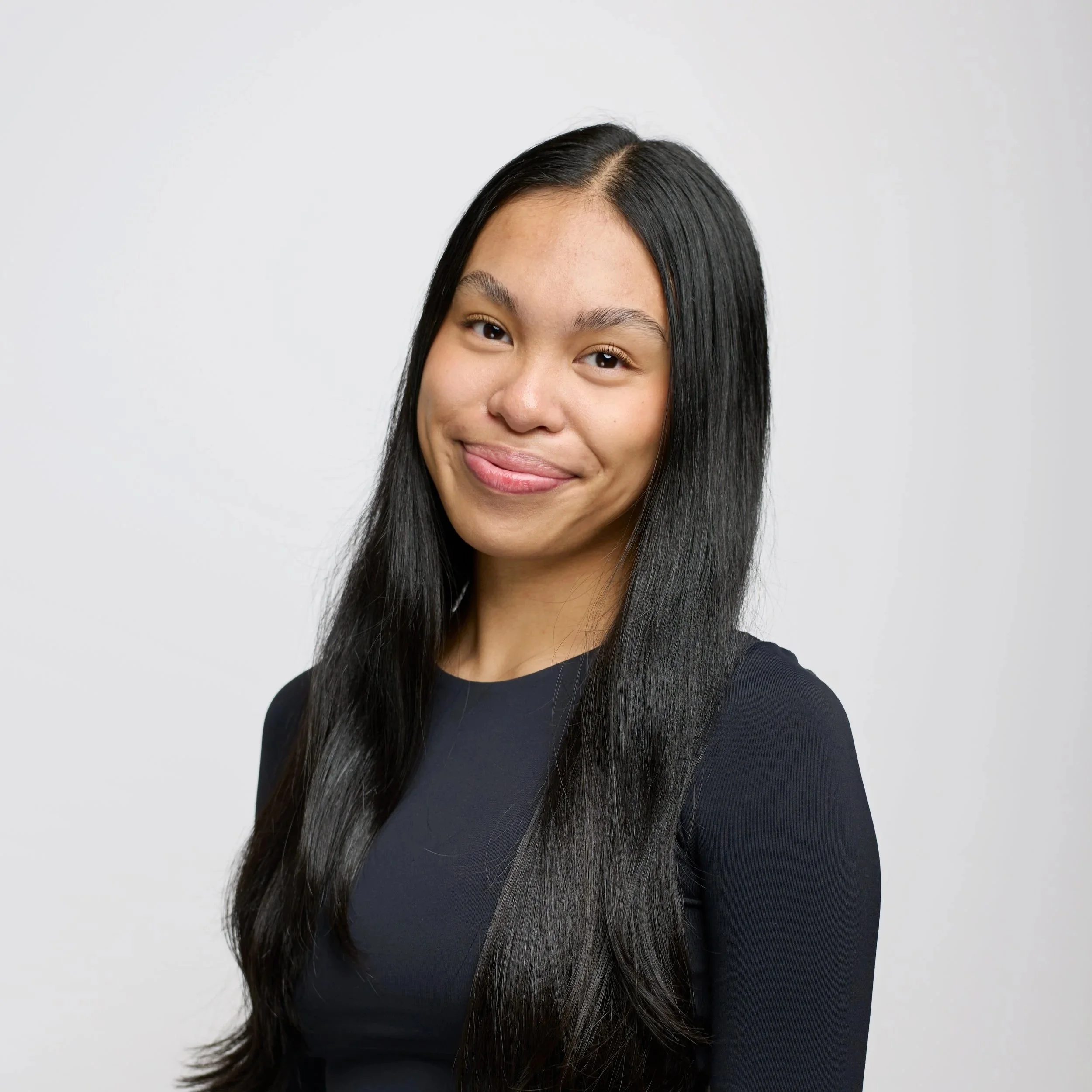 Portrait of a woman with glasses and dreadlocks, wearing a black top, smiling against a black background.