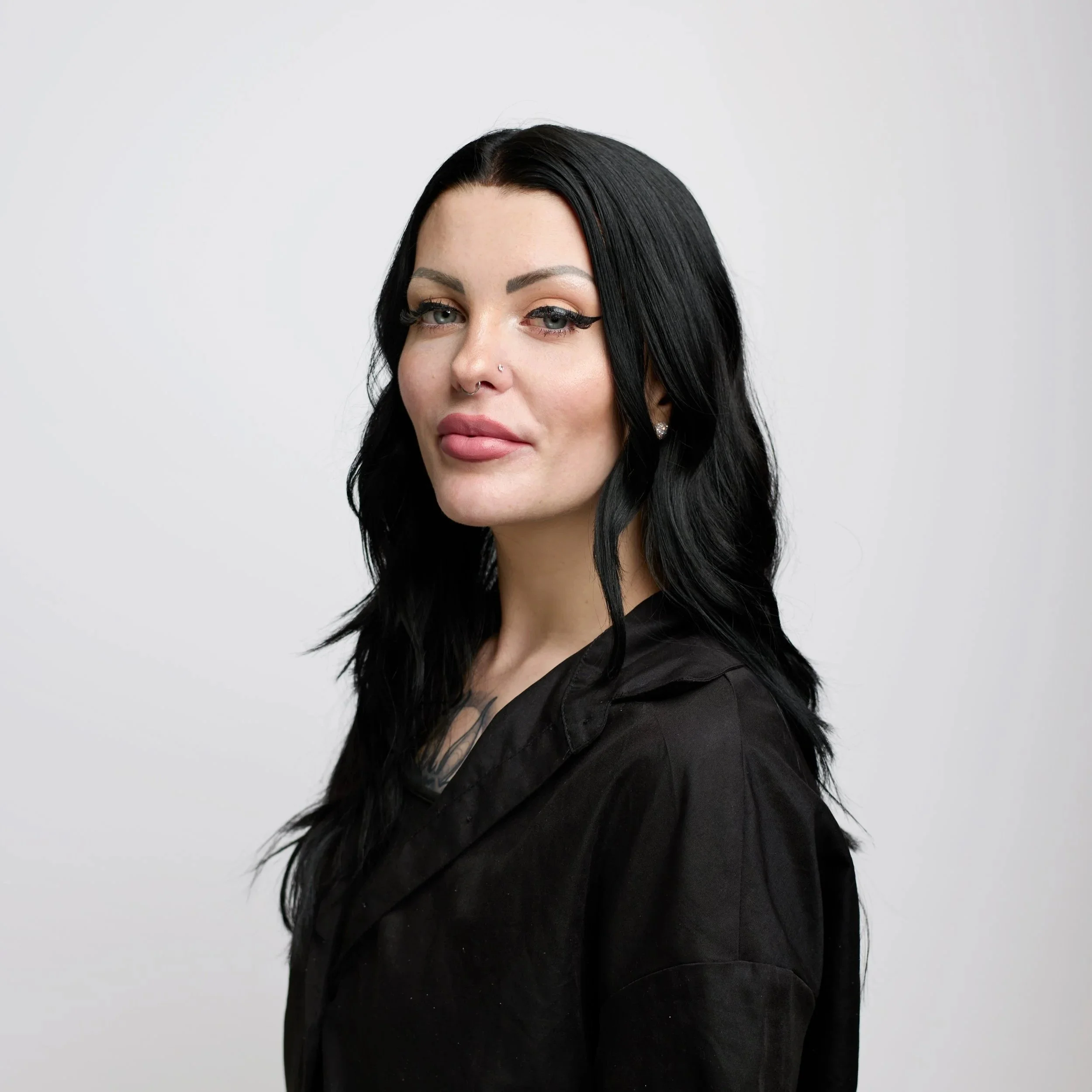 A young man with curly hair and facial hair wearing a white button-up shirt, looking at the camera against a black background.